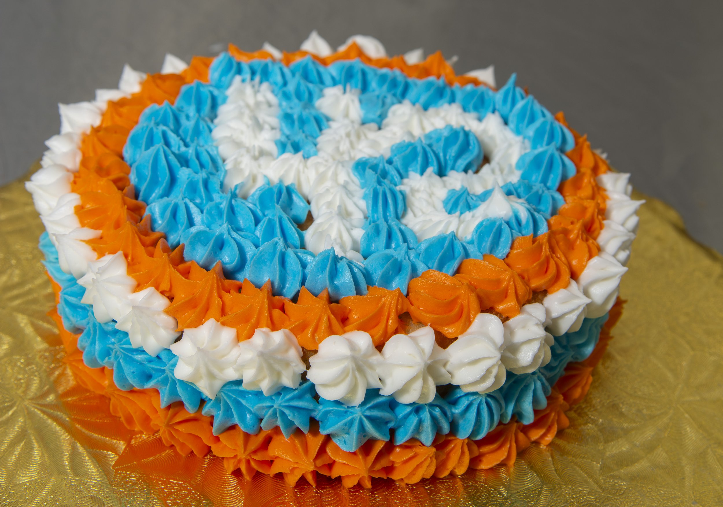 Decorative round cake with piped blue, white, and orange frosting arranged in a pattern.