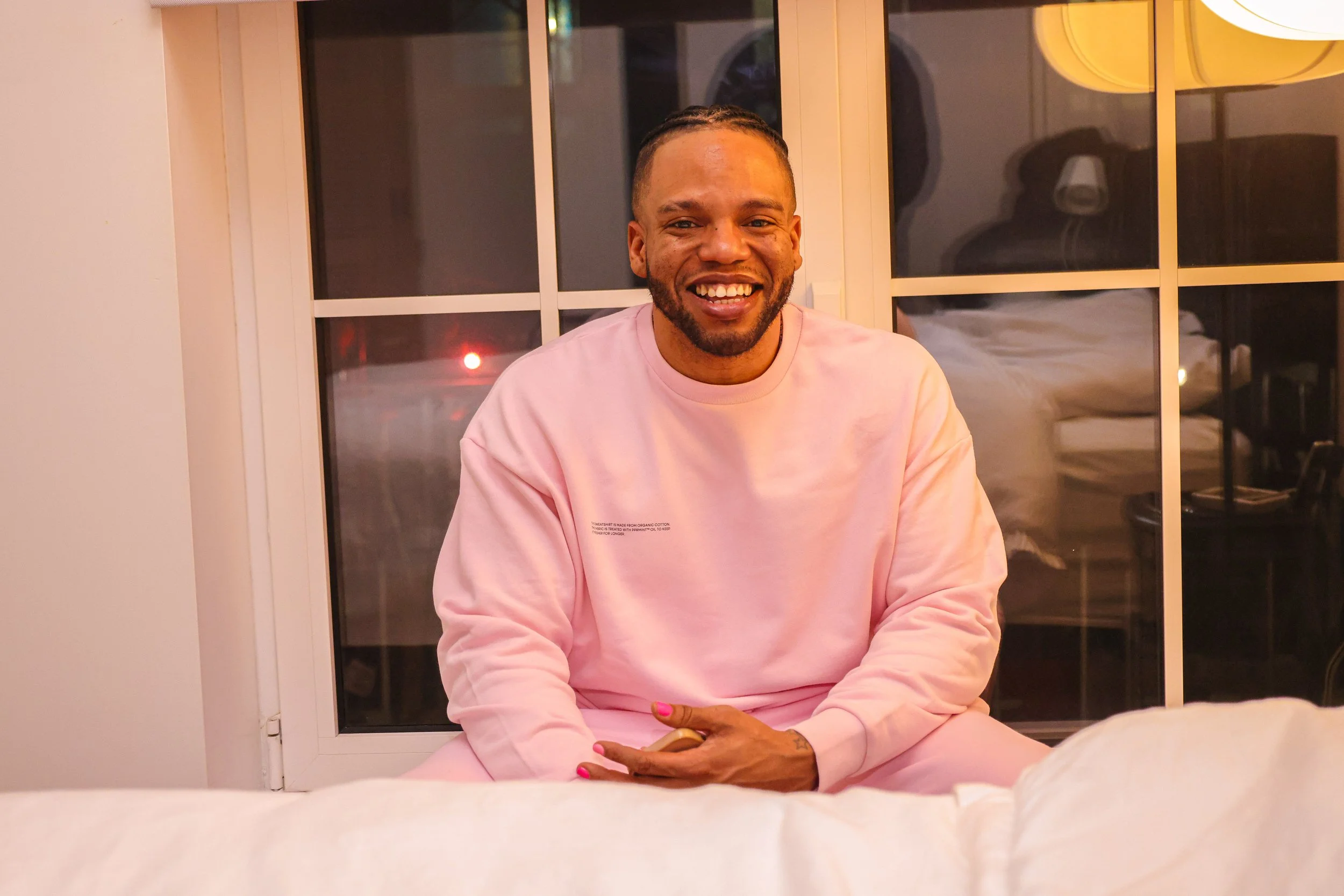 Kareem youngblood sitting in bedroom window in a pink sweat suit with pink fingernails