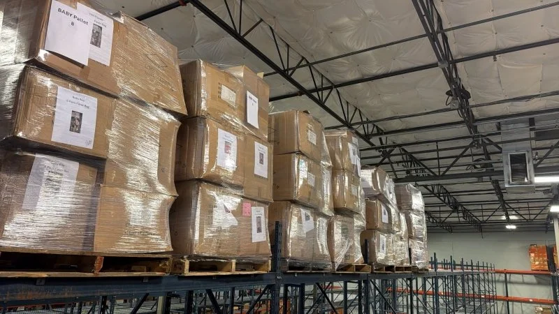 Stacks of large cardboard boxes wrapped in plastic on pallets in a warehouse.