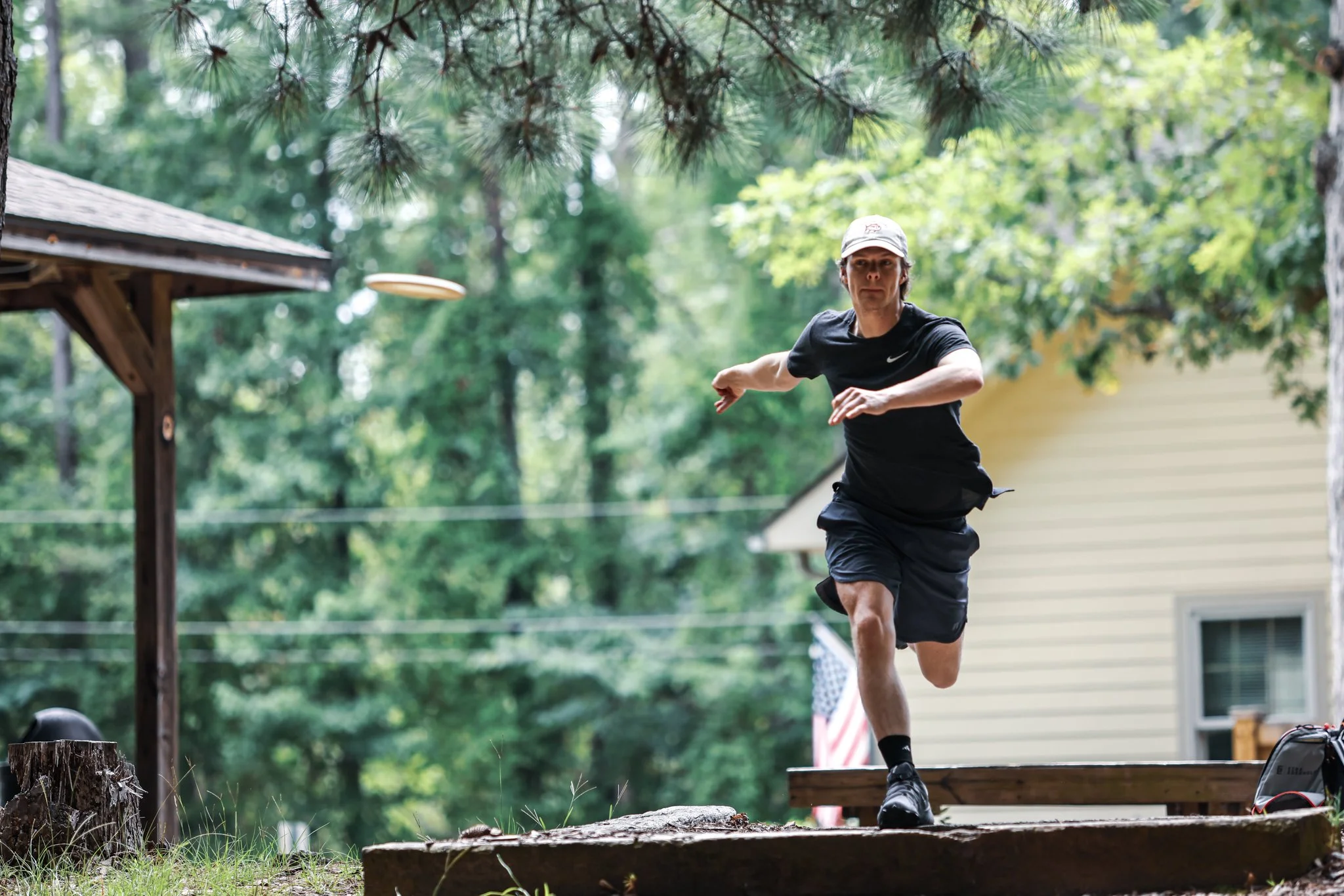 A person in athletic clothing throws a frisbee outdoors in a wooded area.
