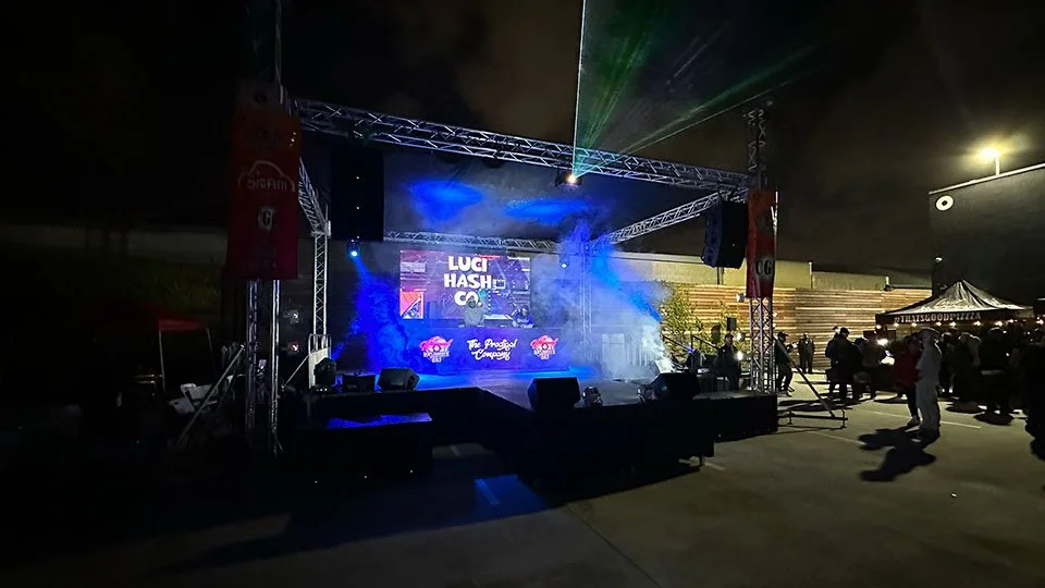 ProWall LED Wall Rental Nighttime outdoor concert stage with blue and green laser lights, large screen displaying text, and around 20 people gathered around near tents and seating.