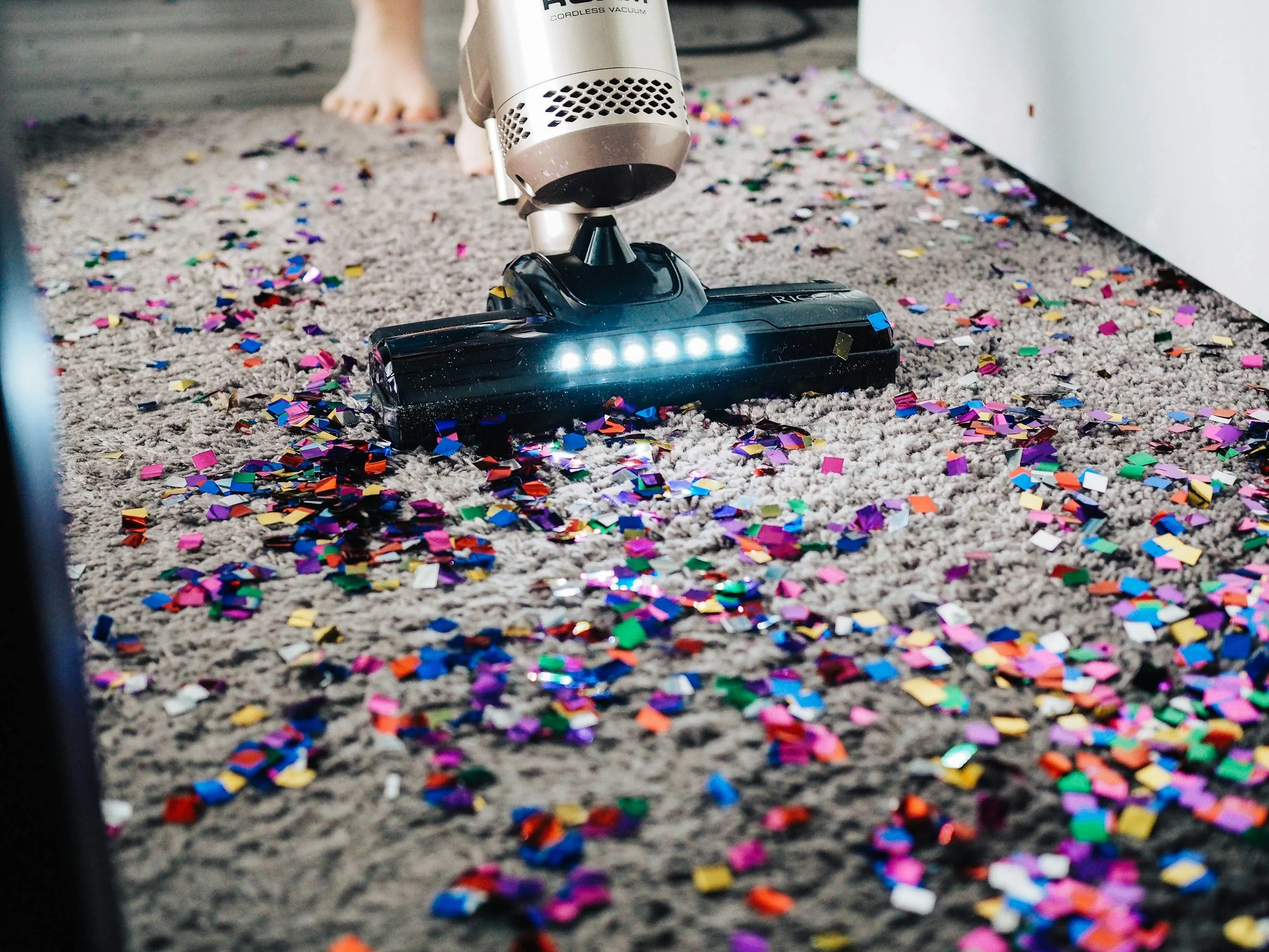 Vacuum cleaner picking up colorful confetti from carpet