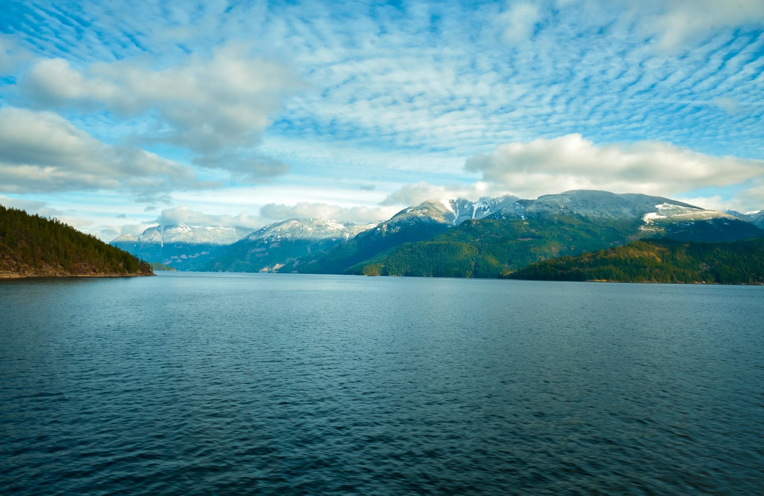 Scenic view of a lake with surrounding wooded mountains and a partly cloudy sky.