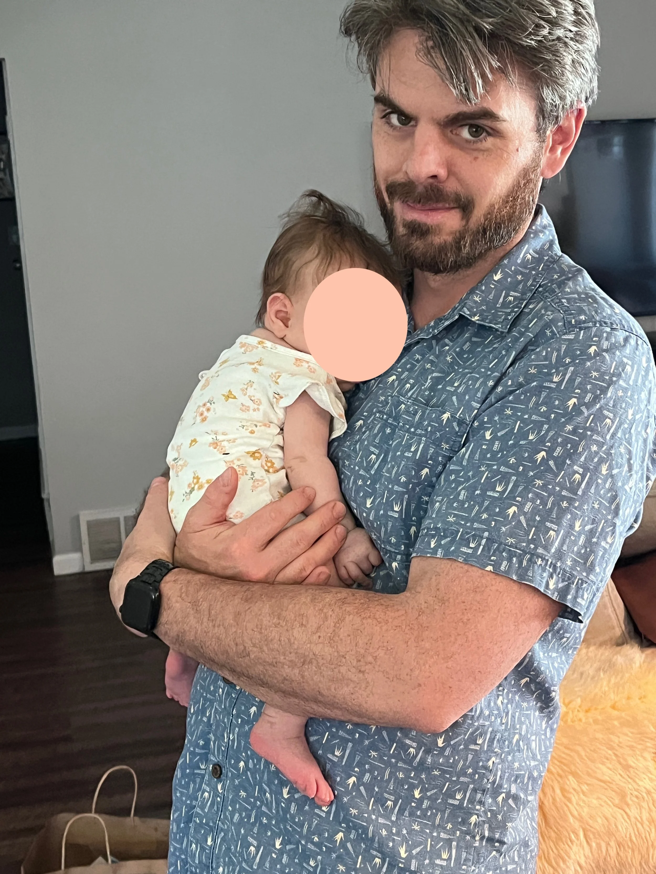Caucasian male with a beard holding a baby with the face covered.