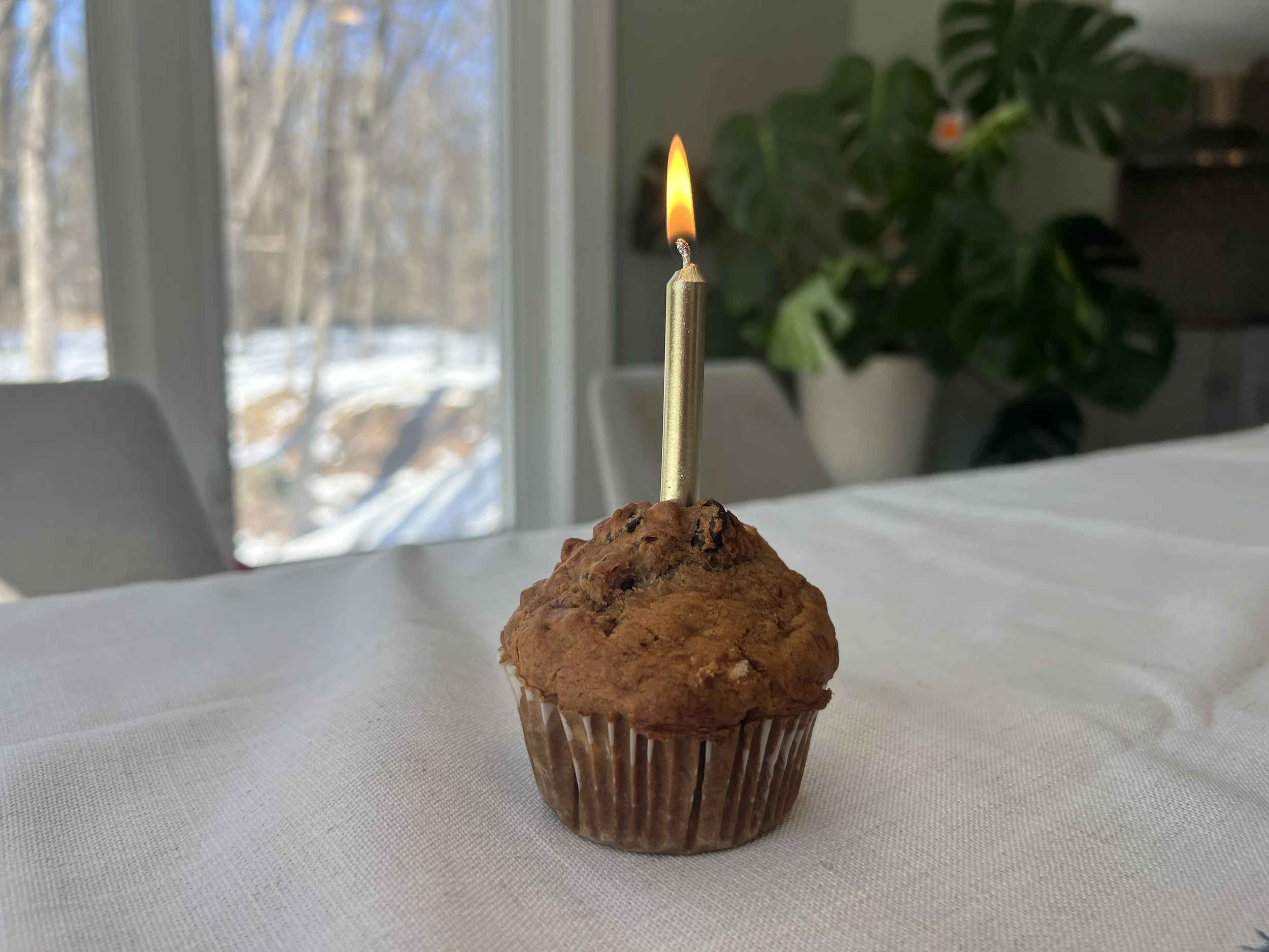Muffin with a birthday candle on a table with a white table cloth