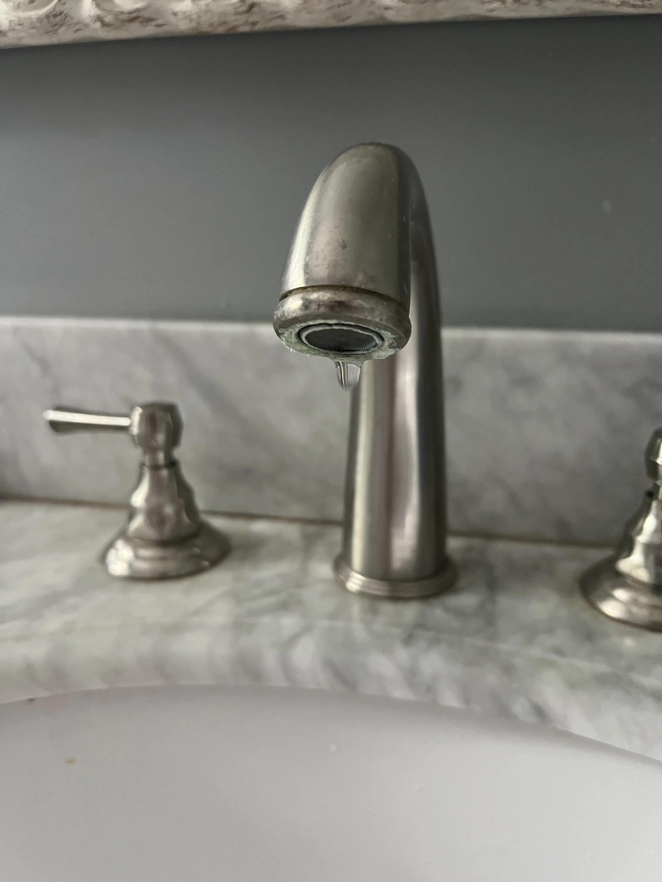 A silver faucet with a slow leak on a marble countertop