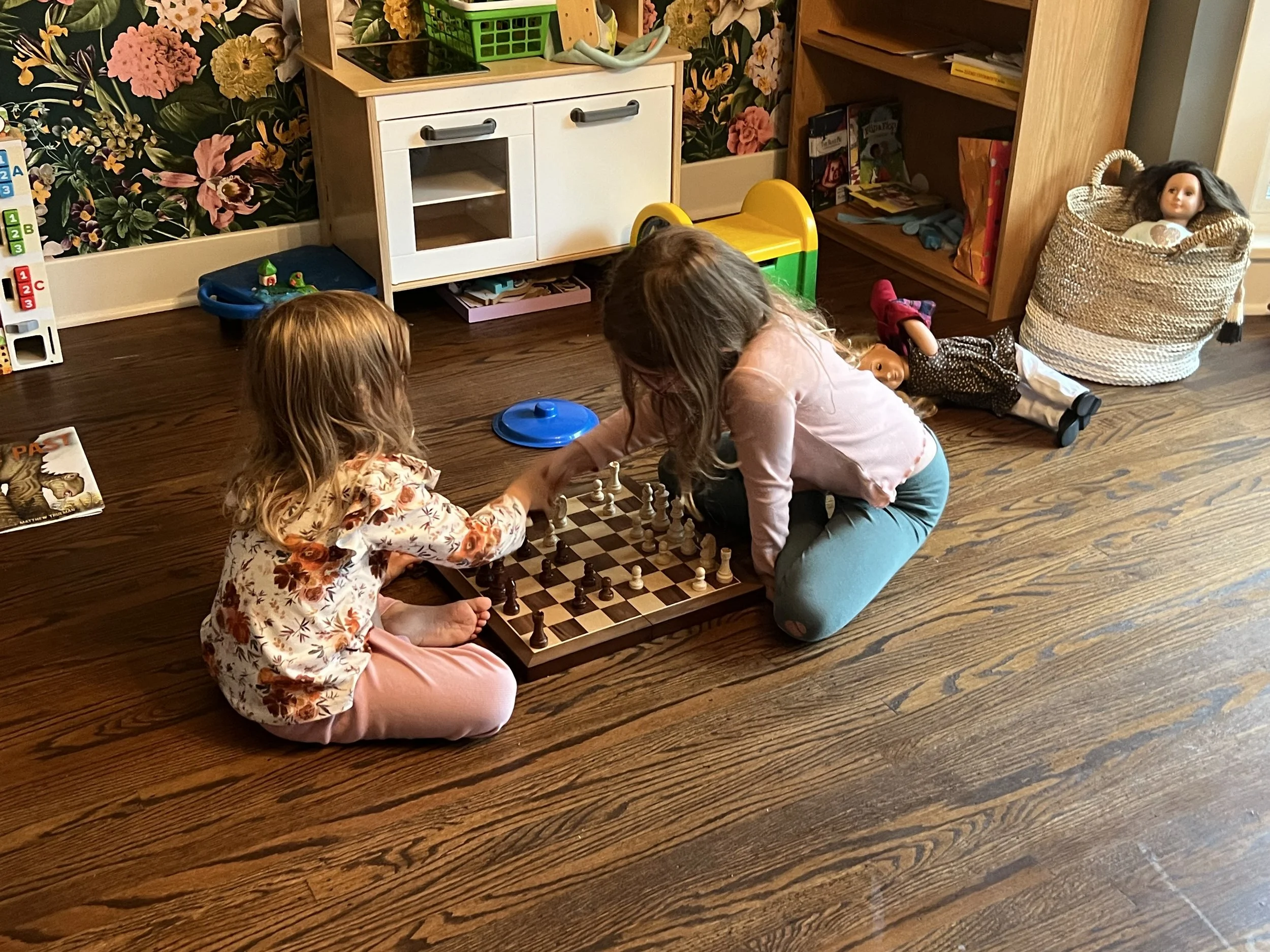 Two girls playing chess on the floor.