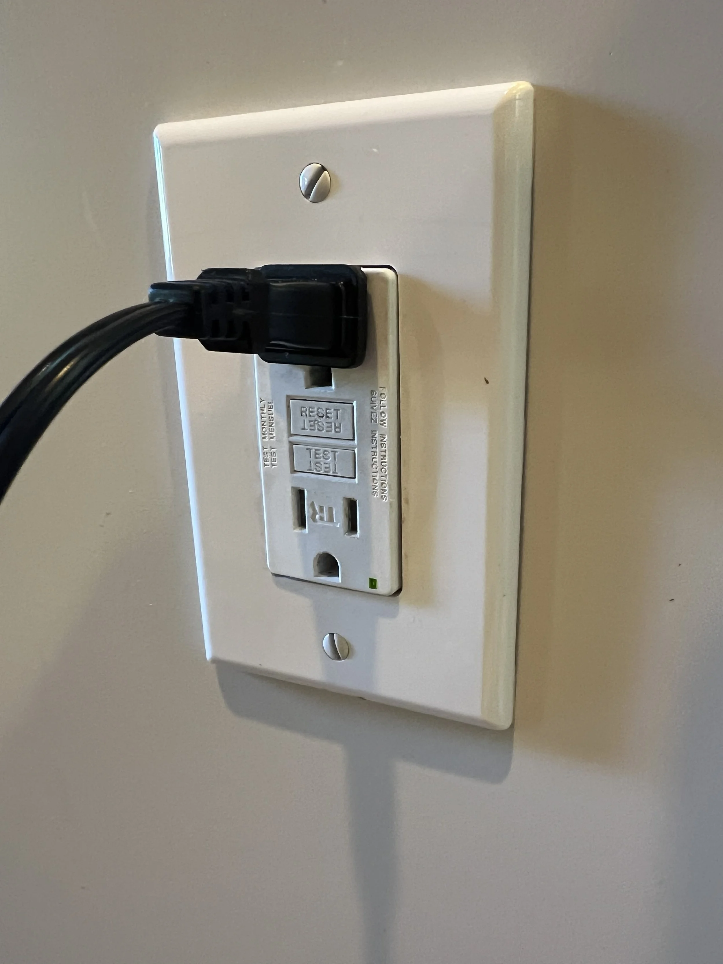 A black power cord plugged into a white outlet