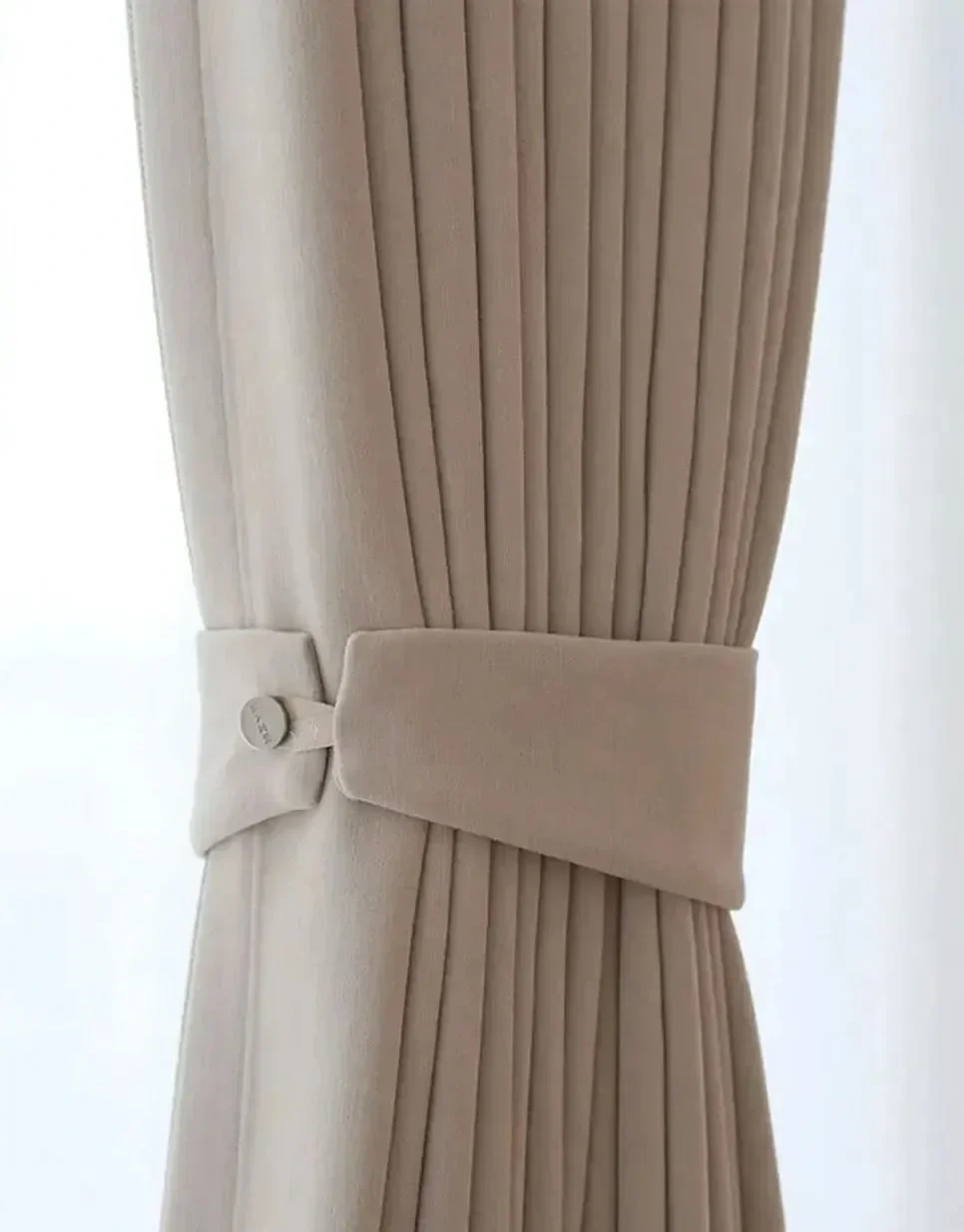 A close-up of beige curtains with pleats, tied back with a matching fabric tie, and a button with the word 'PANEL' on it.