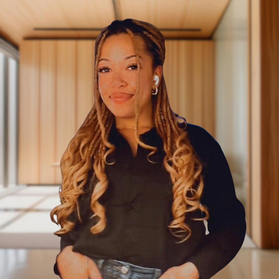 A woman with long, curled hair wearing a black shirt and blue jeans, standing in a wooden interior space.