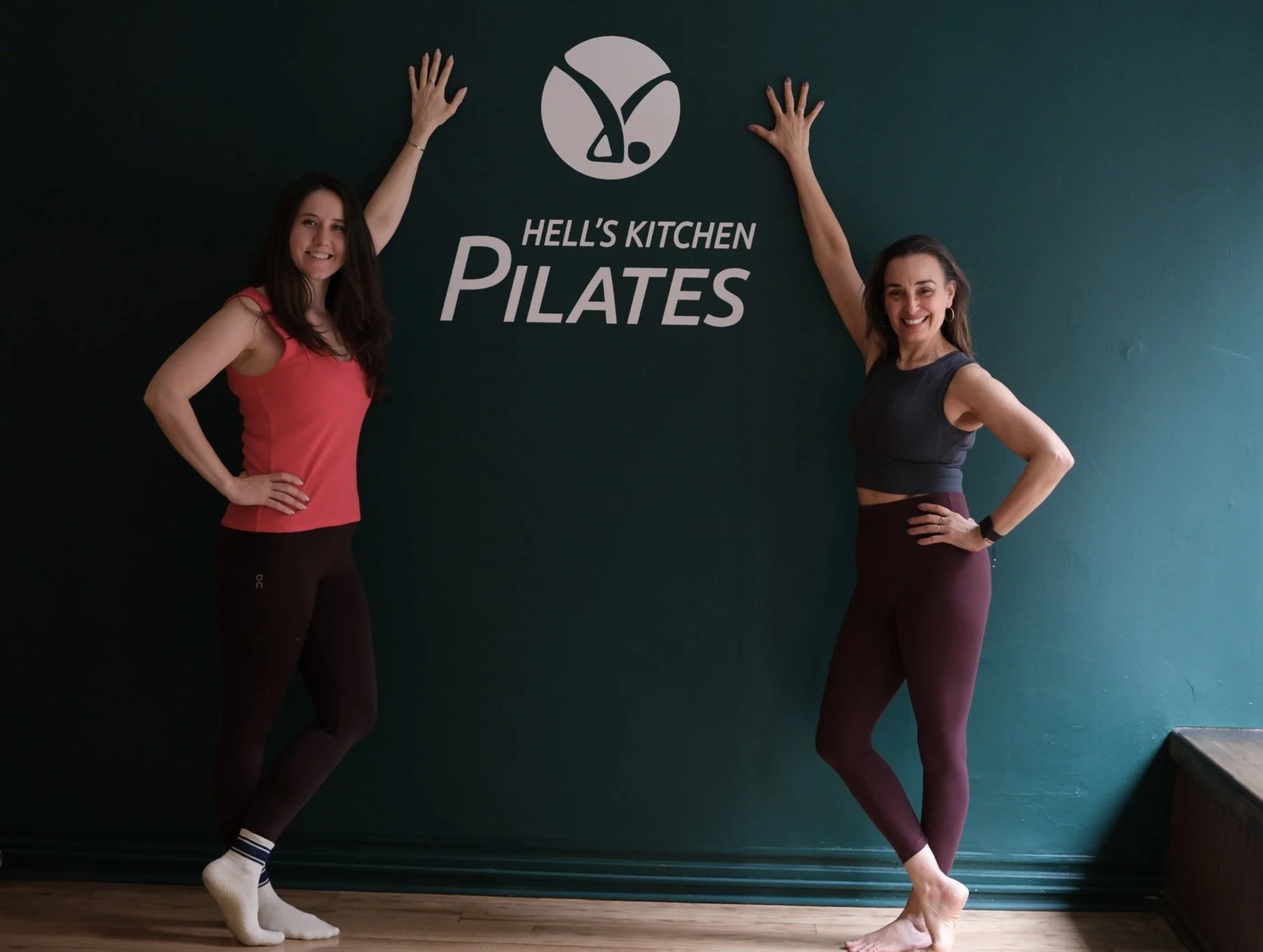 Hell's Kitchen Pilates founders Kim and Nadya posing in front of the studio logo in NYC.