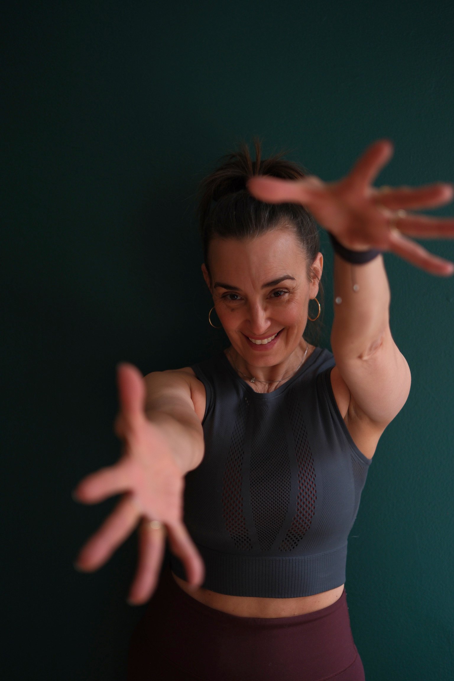 Kim Villanueva, Pilates studio owner at Hell's Kitchen Pilates, smiling and reaching forward.