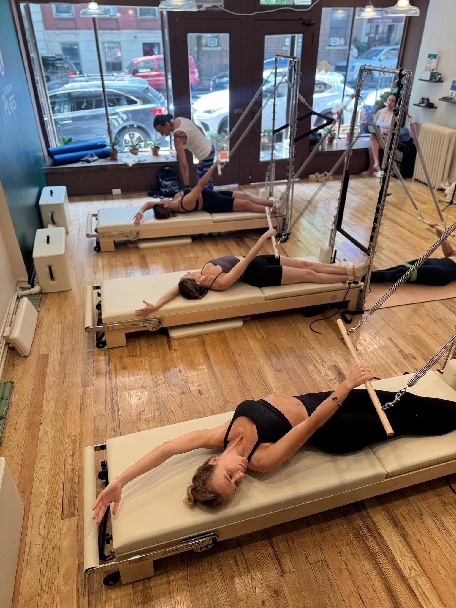 Overhead view of clients testing different Elina Pilates reformers during an equipment consultation at the Hell's Kitchen Pilates NYC studio.