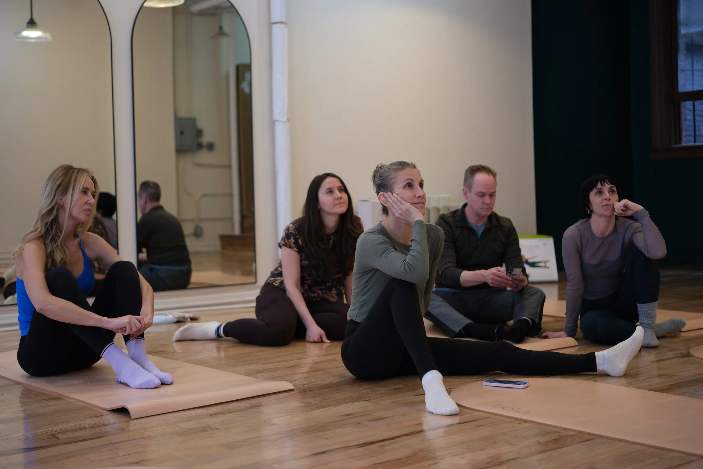 Group of students sitting on mats listening to a lecture during a Pilates anatomy workshop at Hell's Kitchen Pilates.
