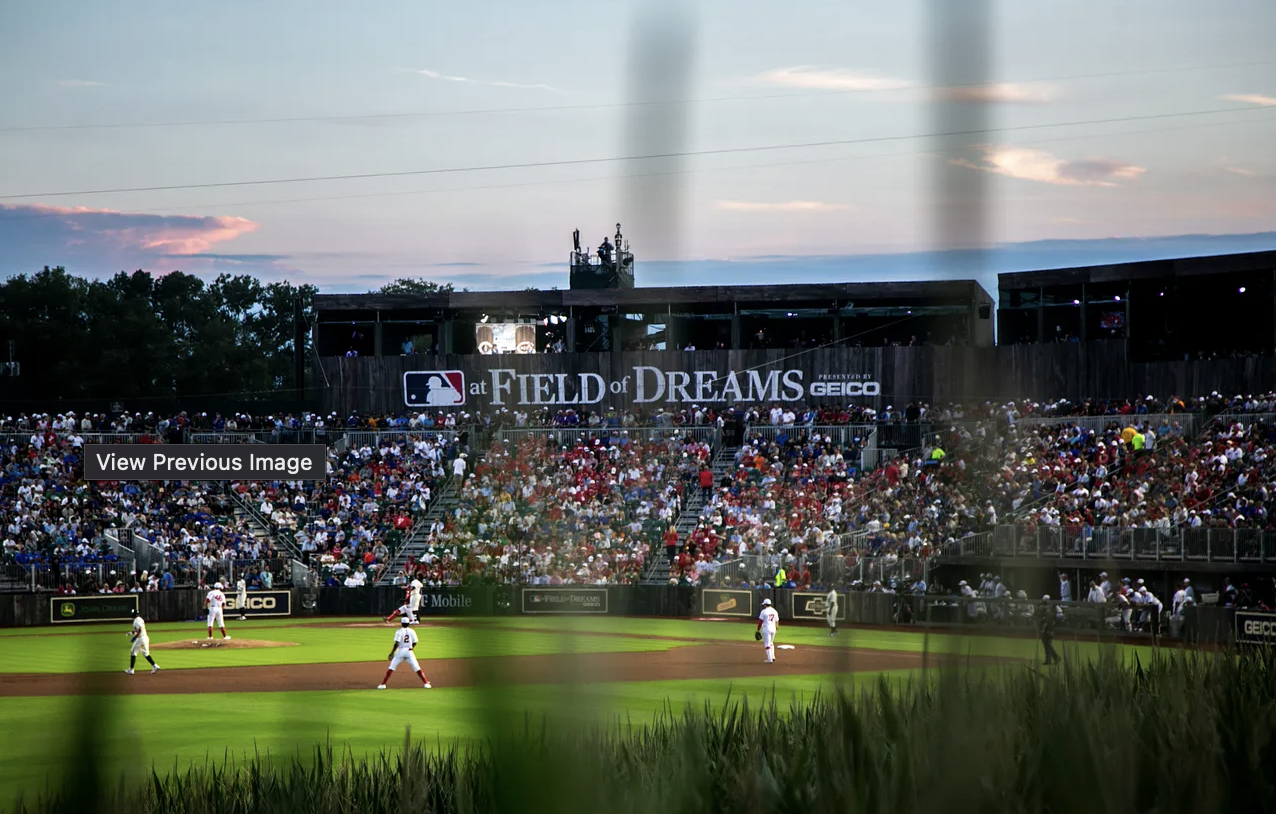 Baseball game at Field of Dreams with players on the field and spectators in the stands during sunset.