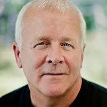 A man with short, light-colored hair wearing dark sunglasses and a black shirt.