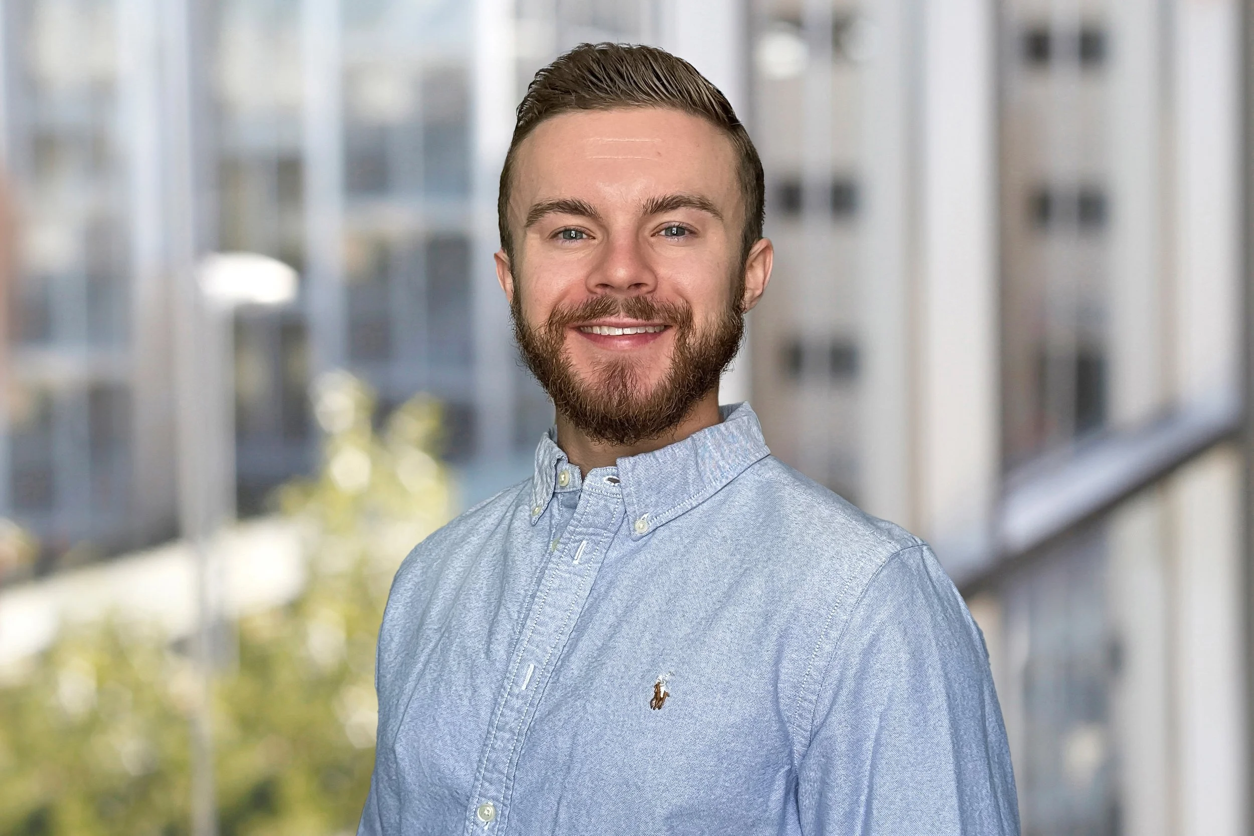 A smiling young man with short hair and a beard, wearing a collared shirt.