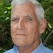 A photo of a older man with gray hair, wearing a collared shirt.