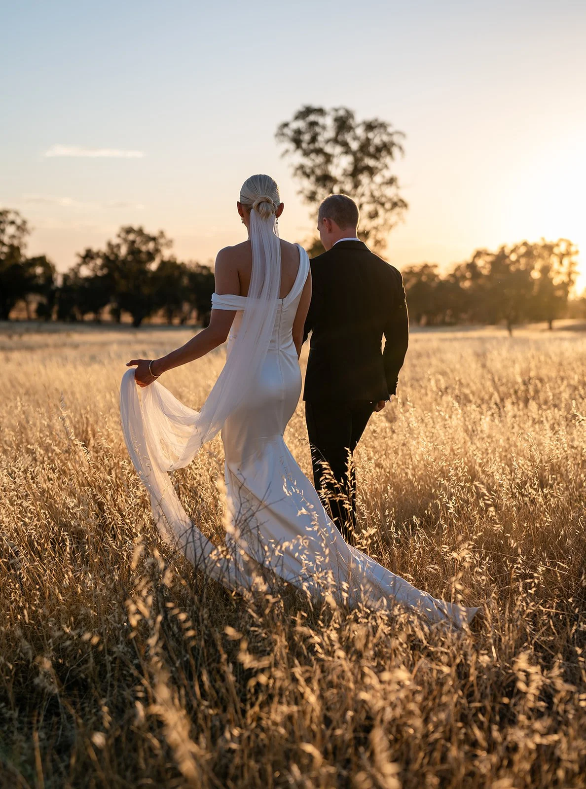 Bride and groom walking through a picturesque pasture paddock at sunset at Rawson Park Homestead near Wagga Wagga, NSW.