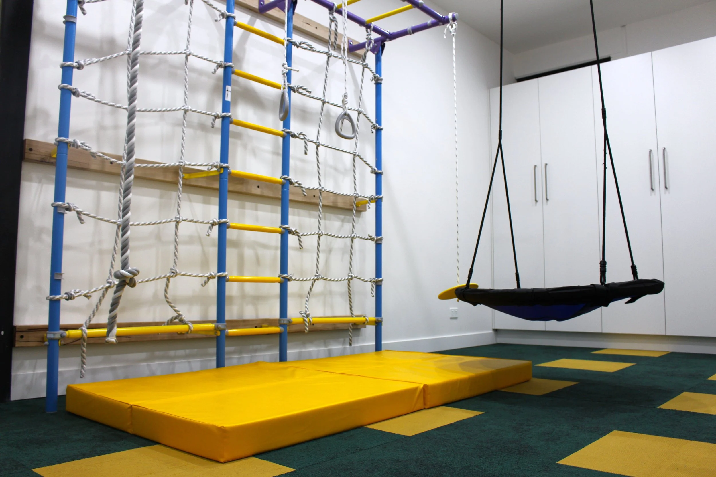 Indoor play area with a climbing wall and a swing in a room with white cabinetry and a green and yellow checkered floor.