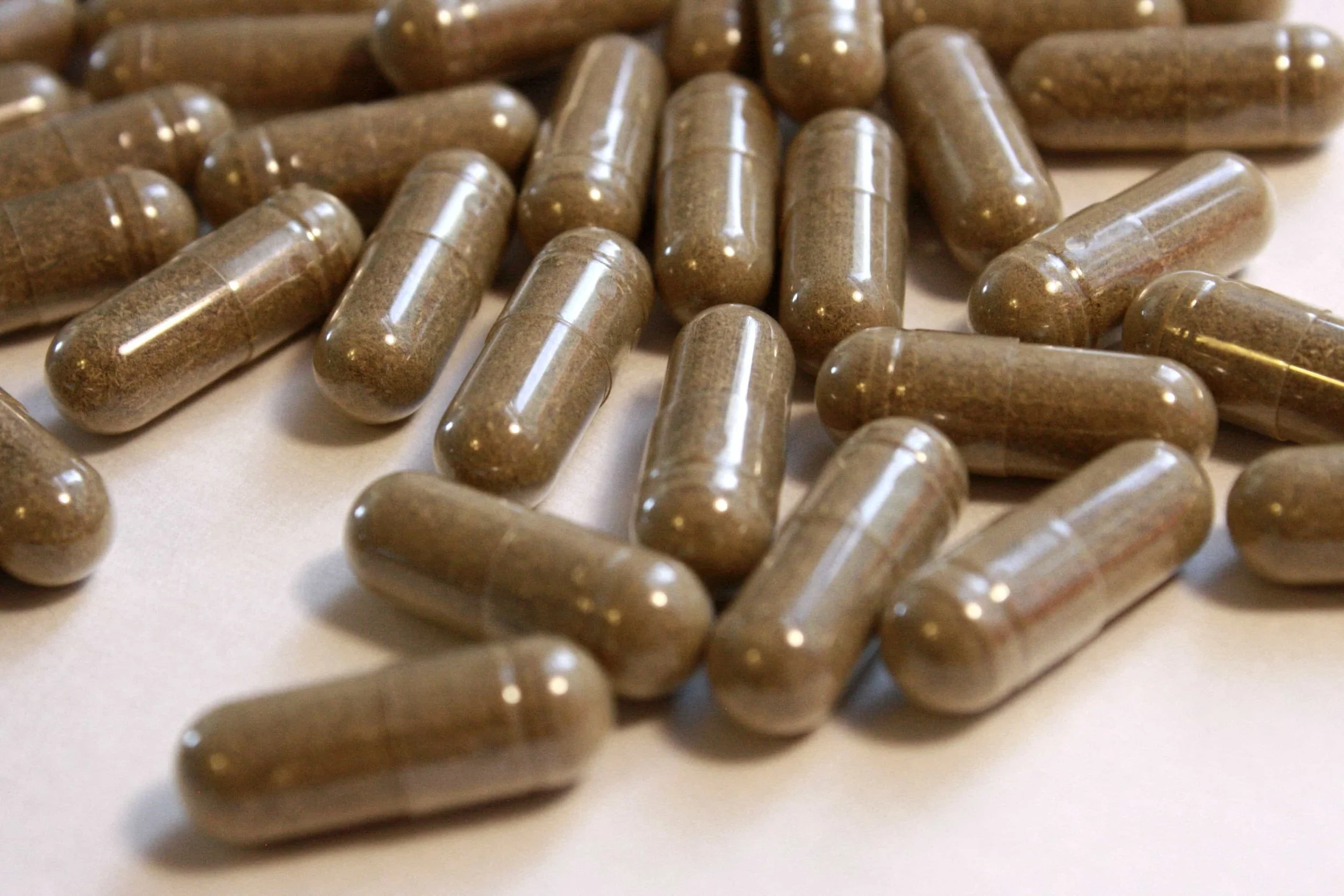 A close-up of numerous brown capsules scattered on a white surface.