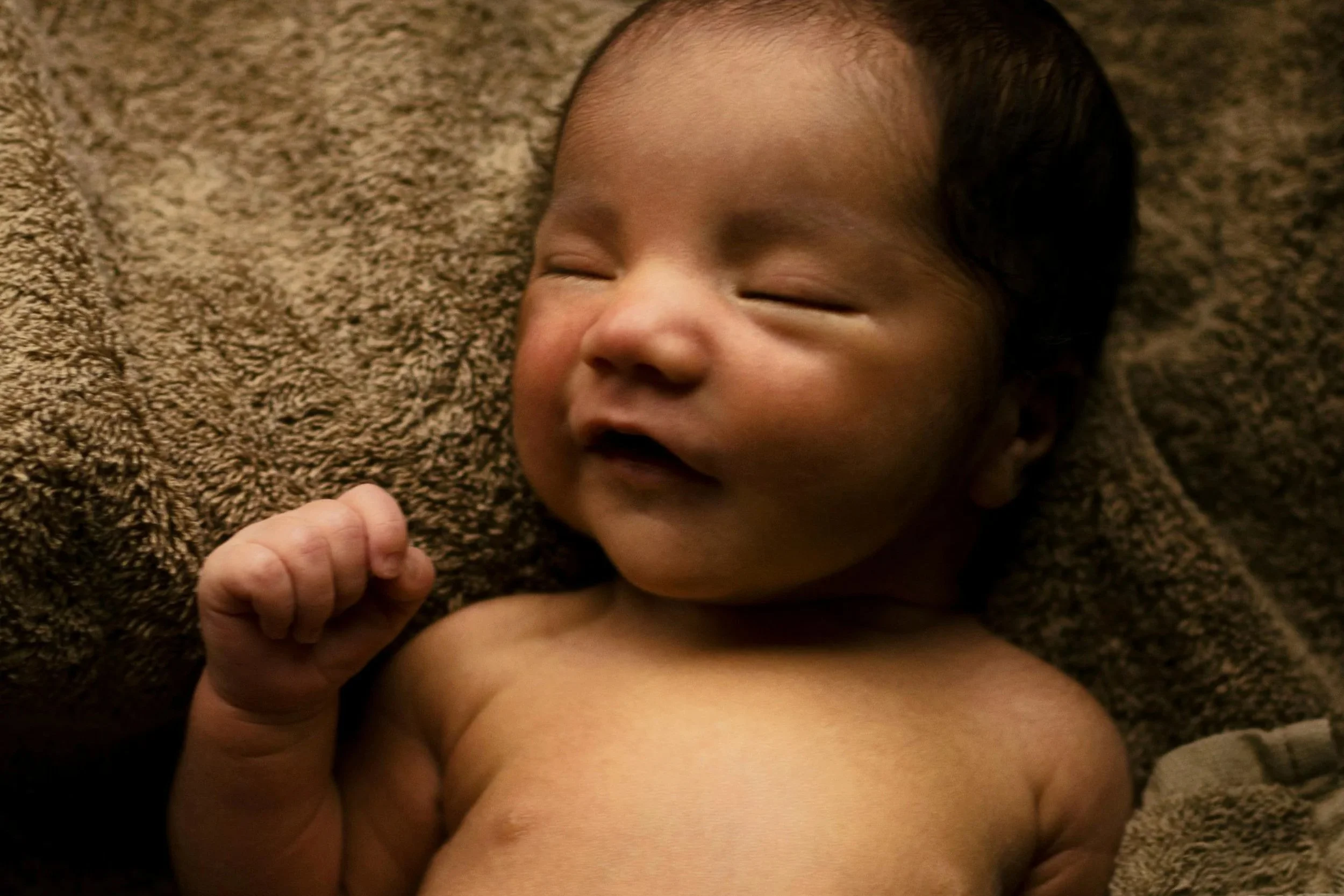 A close-up of a sleeping baby lying on a brown, textured blanket, with one hand near the face.