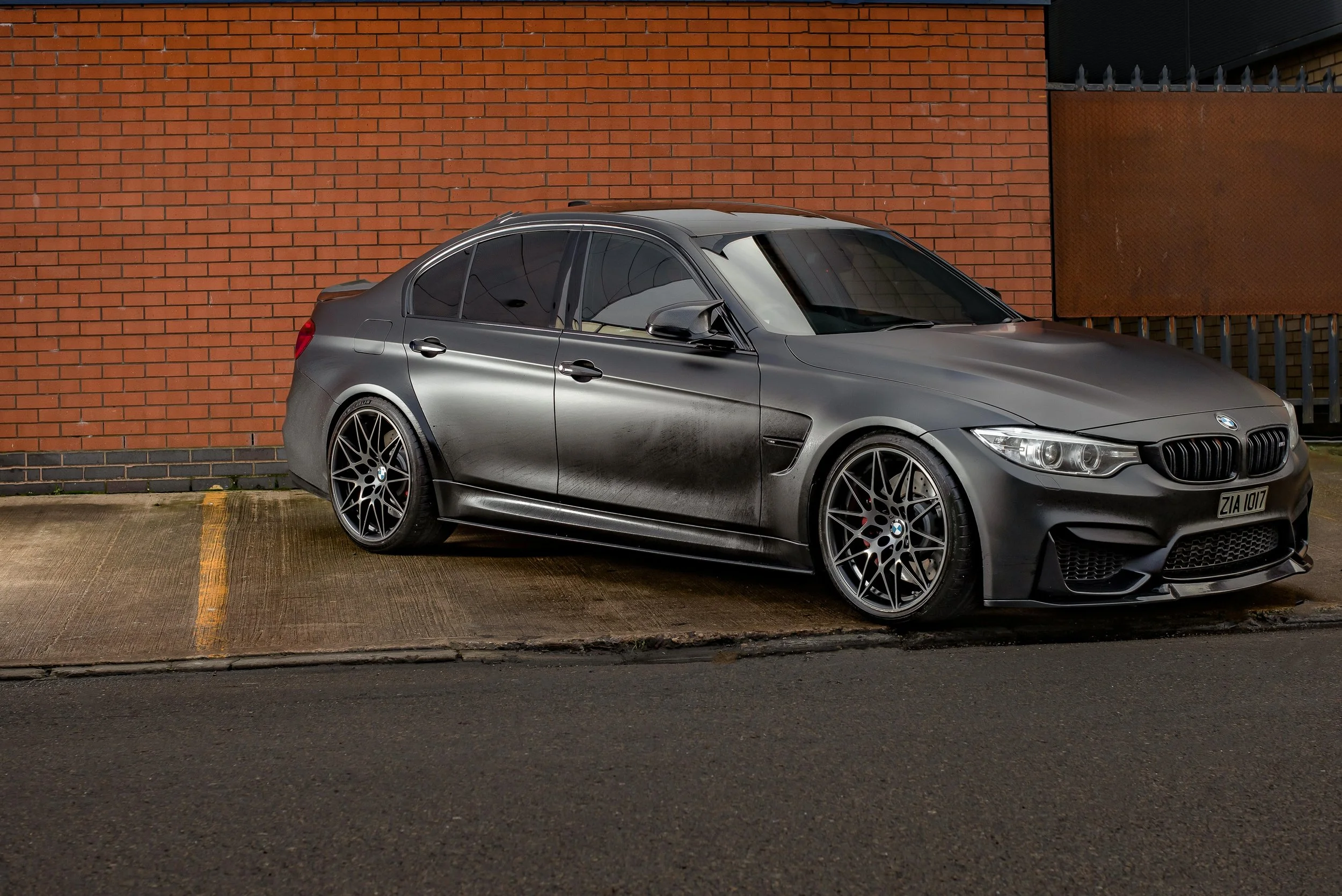 Matte gray sedan car parked in front of a red brick wall.