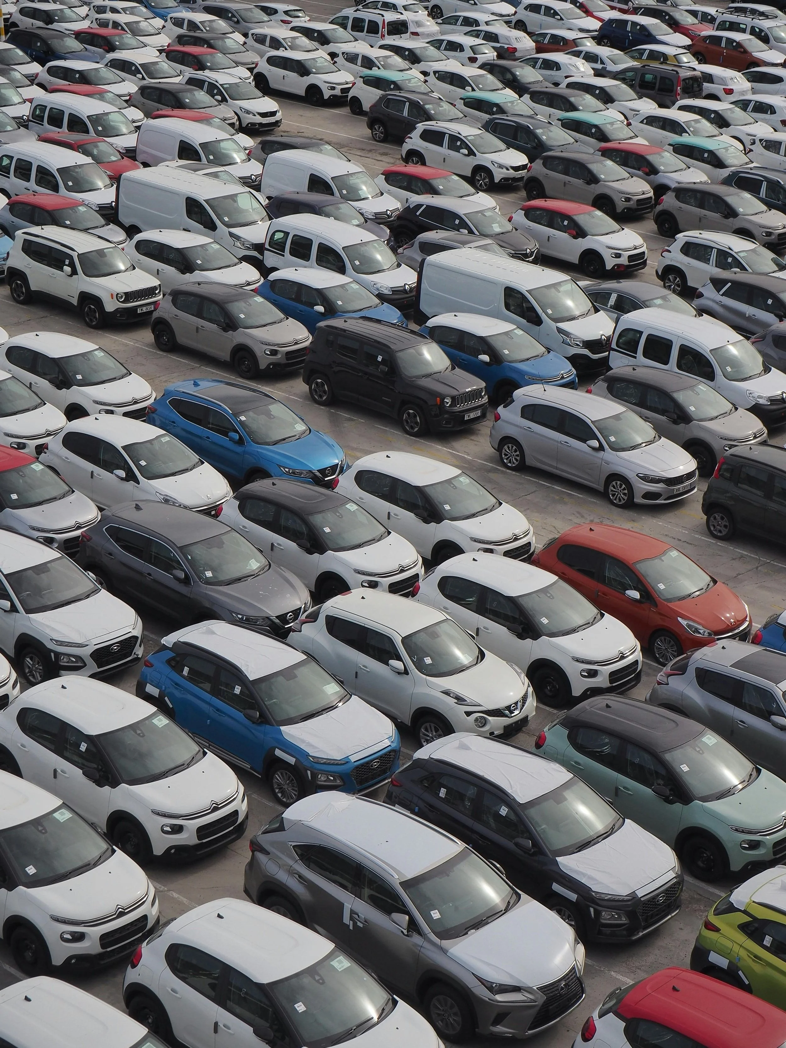A large parking lot filled with various cars and vans, organized in rows.