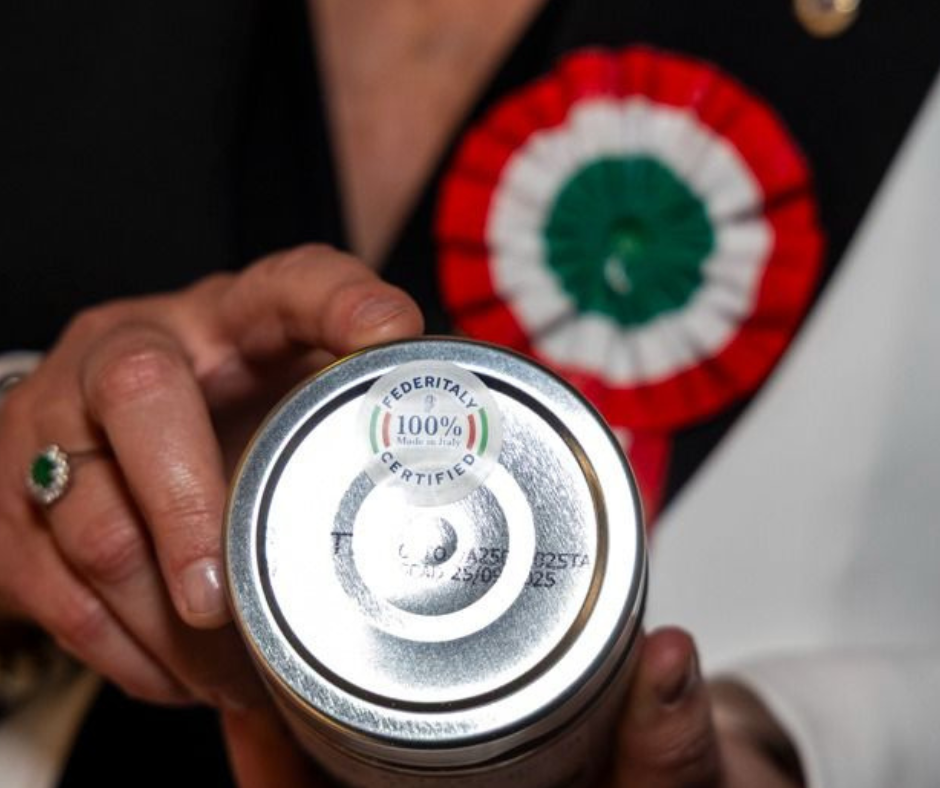 Una persona tiene in mano una lattina con il fondo visibile, sopra c'è un badge con i colori della bandiera italiana e scritto '100% Made in Italy'.