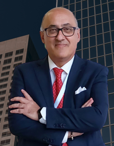 Uomo d'affari con giacca blu, camicia bianca, cravatta rossa con pois, occhiali, sorriso, sfondo urbano con edifici moderni.