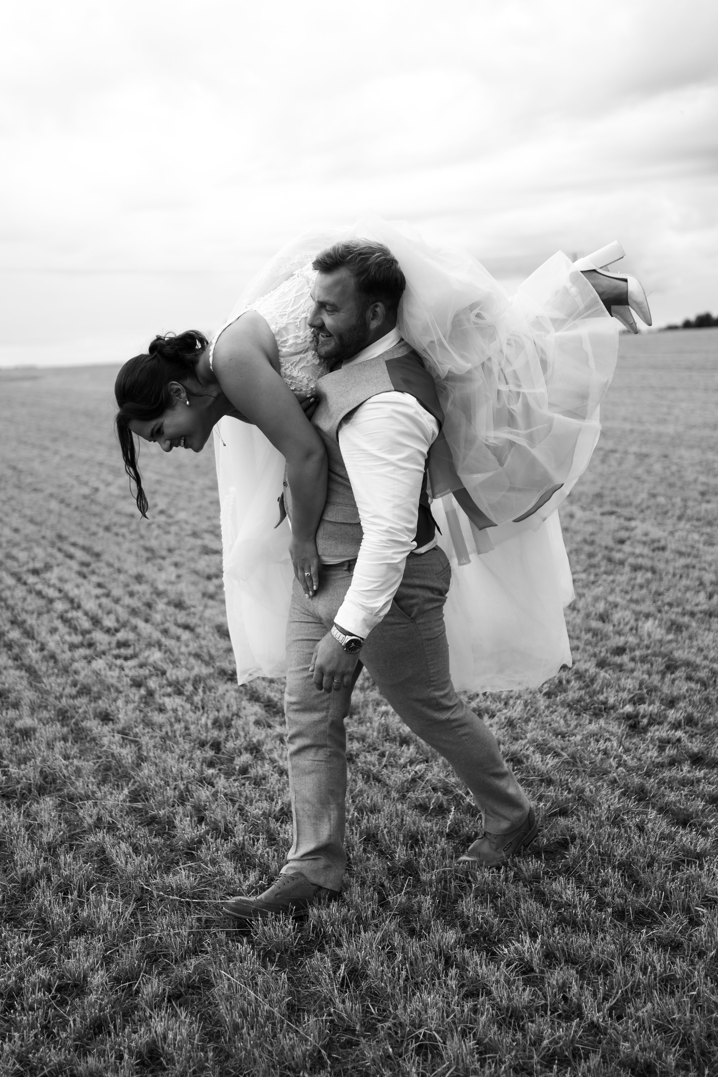 Groom carrying bride on his back in a field, black and white photo
