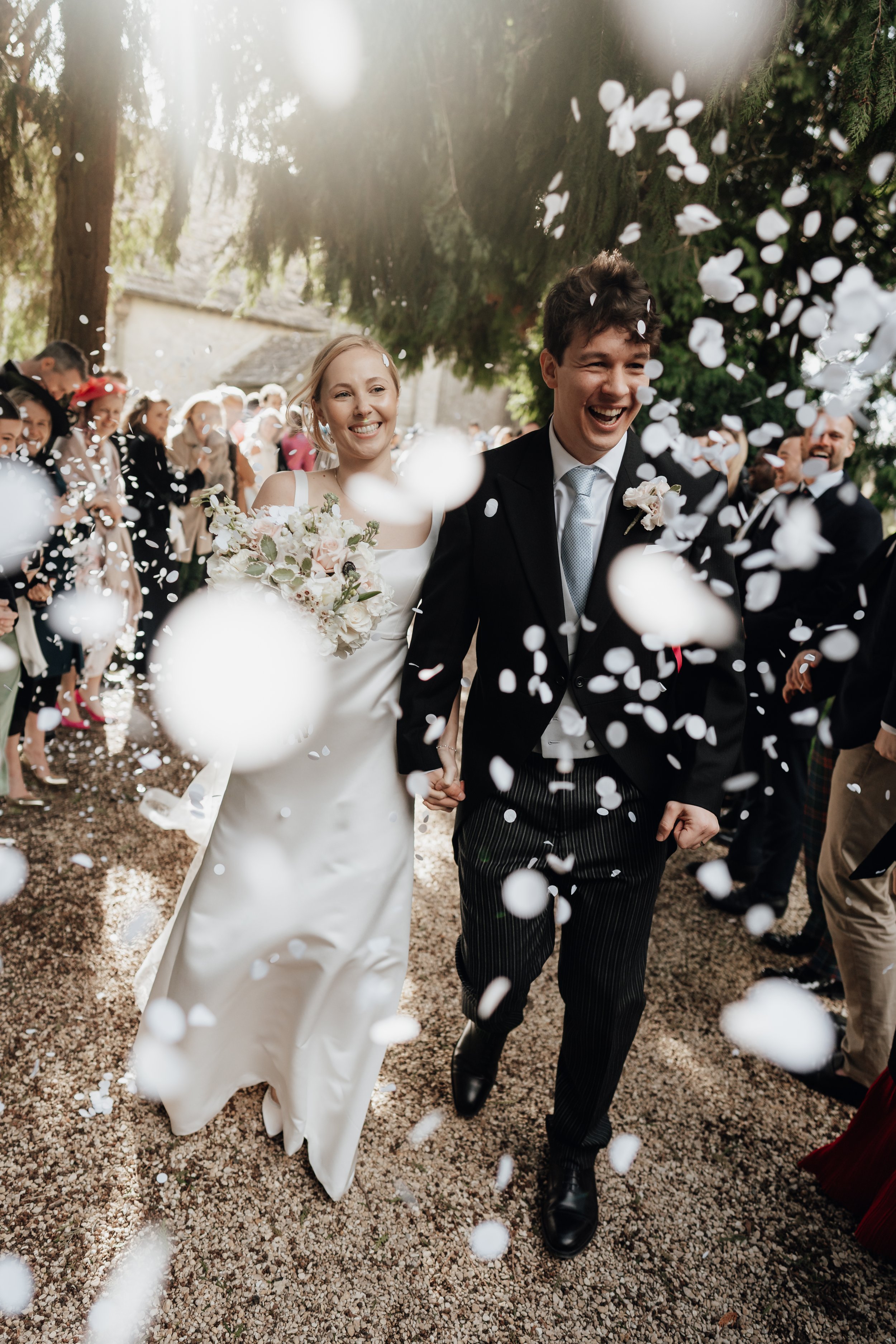 Bride and groom walking through confetti with smiling guests in the background.