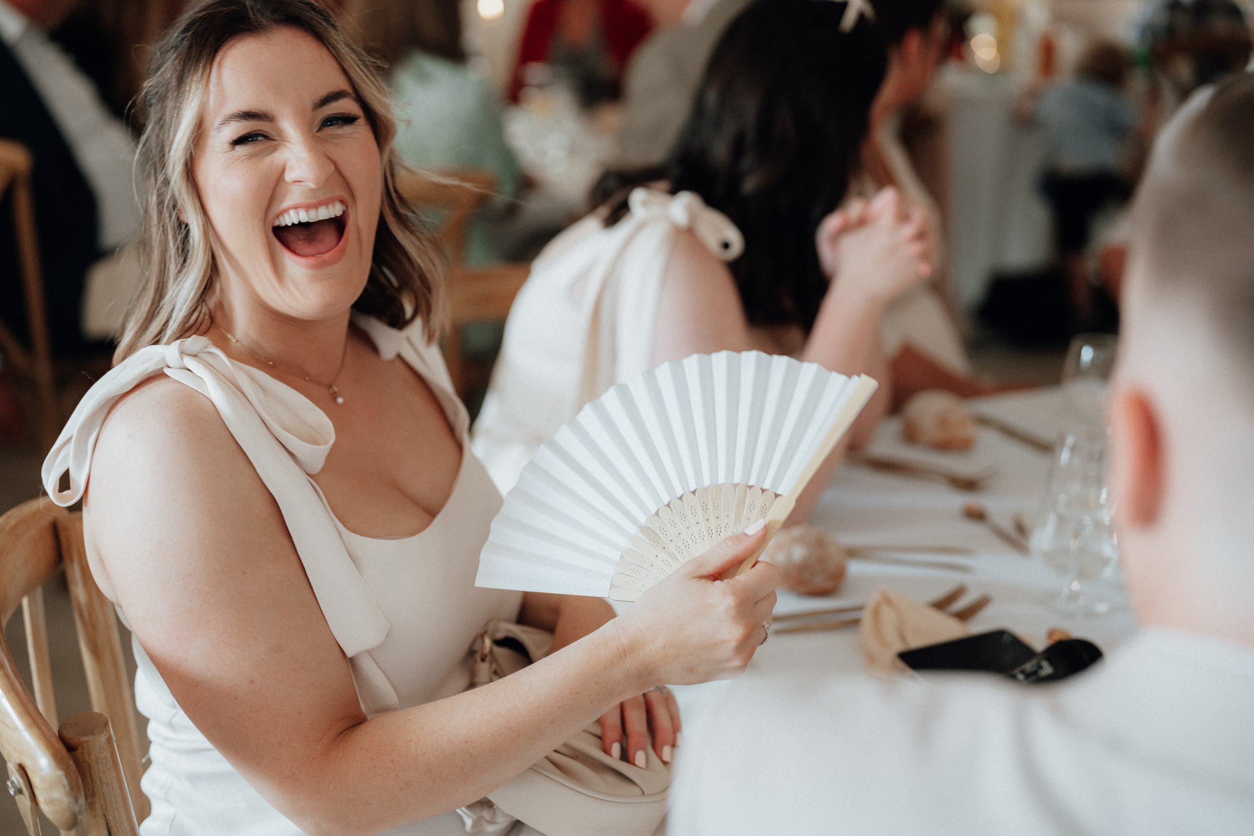 Woman in white holding a hand fan and smiling at a gathering.