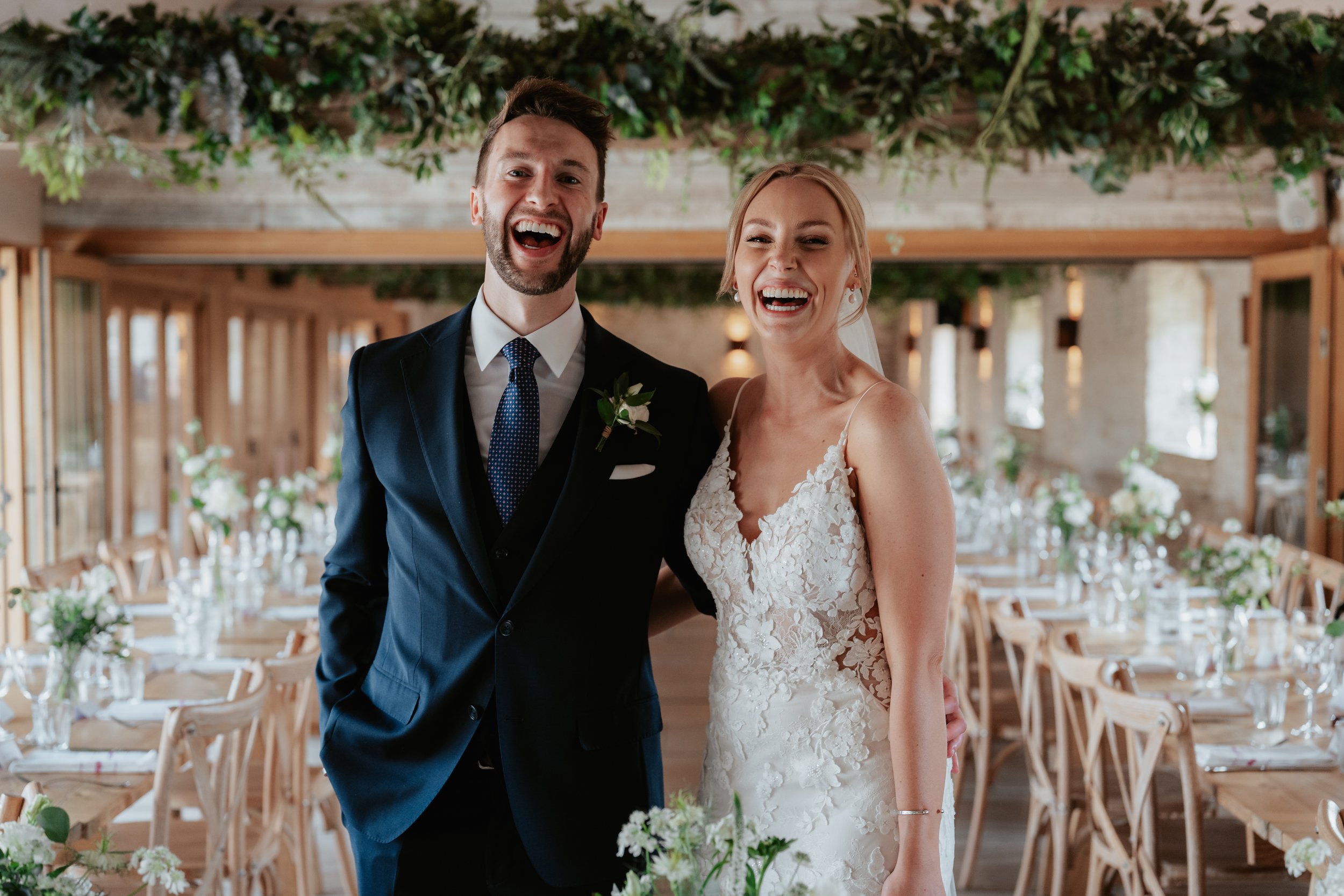 Bride and groom smiling at Old Gore, Cotswolds with flowers and greenery.