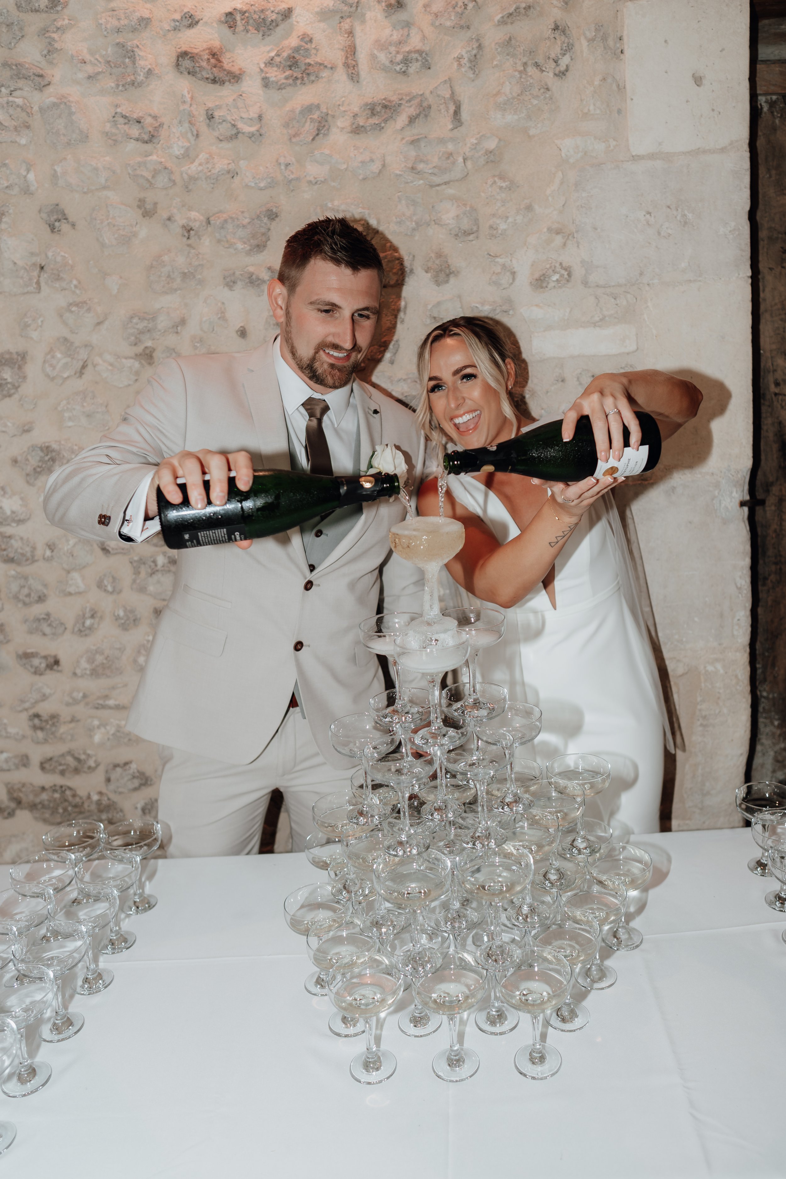 A couple in formal attire pouring champagne into a tower of glasses during a celebration.