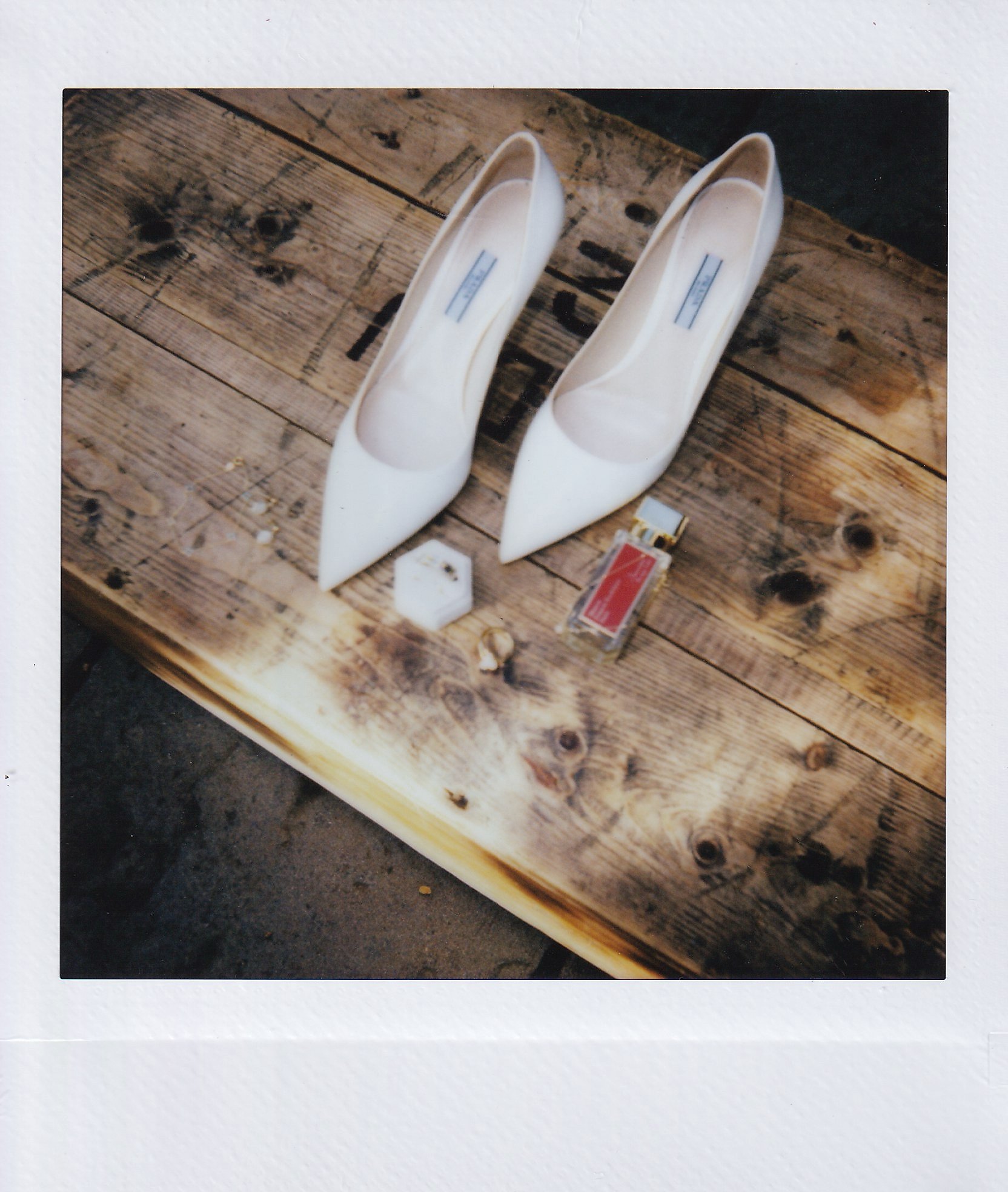 White high-heeled shoes, perfume bottle, and jewelry box on wooden surface.