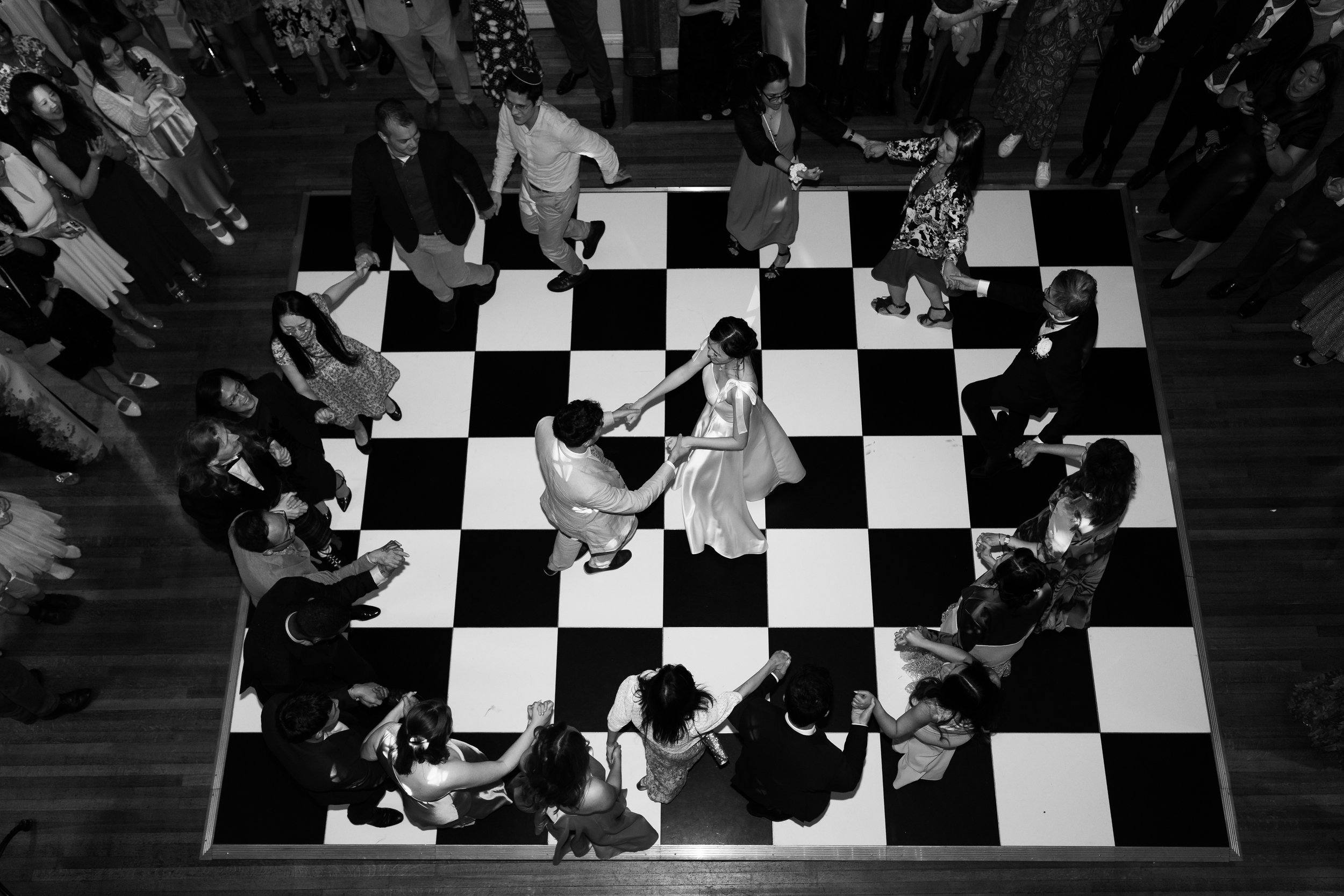 Overhead view of people dancing in a circle at Hedsor House on a black-and-white checkered floor.