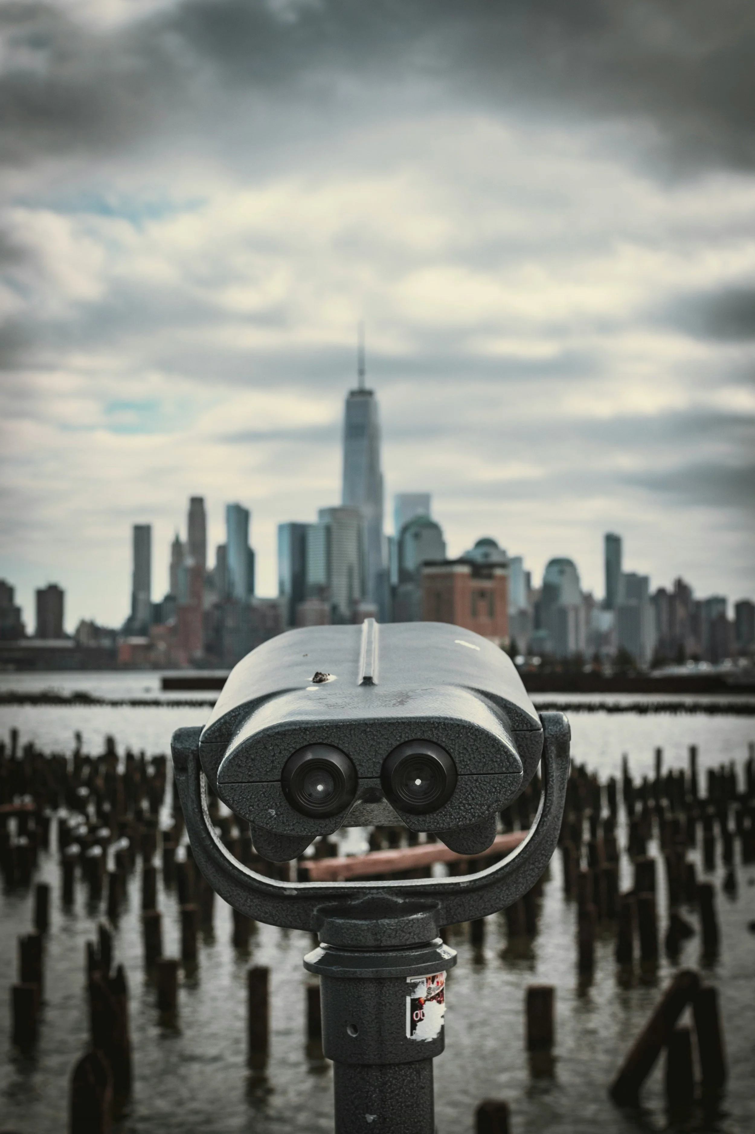 Coin-operated telescope overlooking New York City skyline with One World Trade Center in the background.