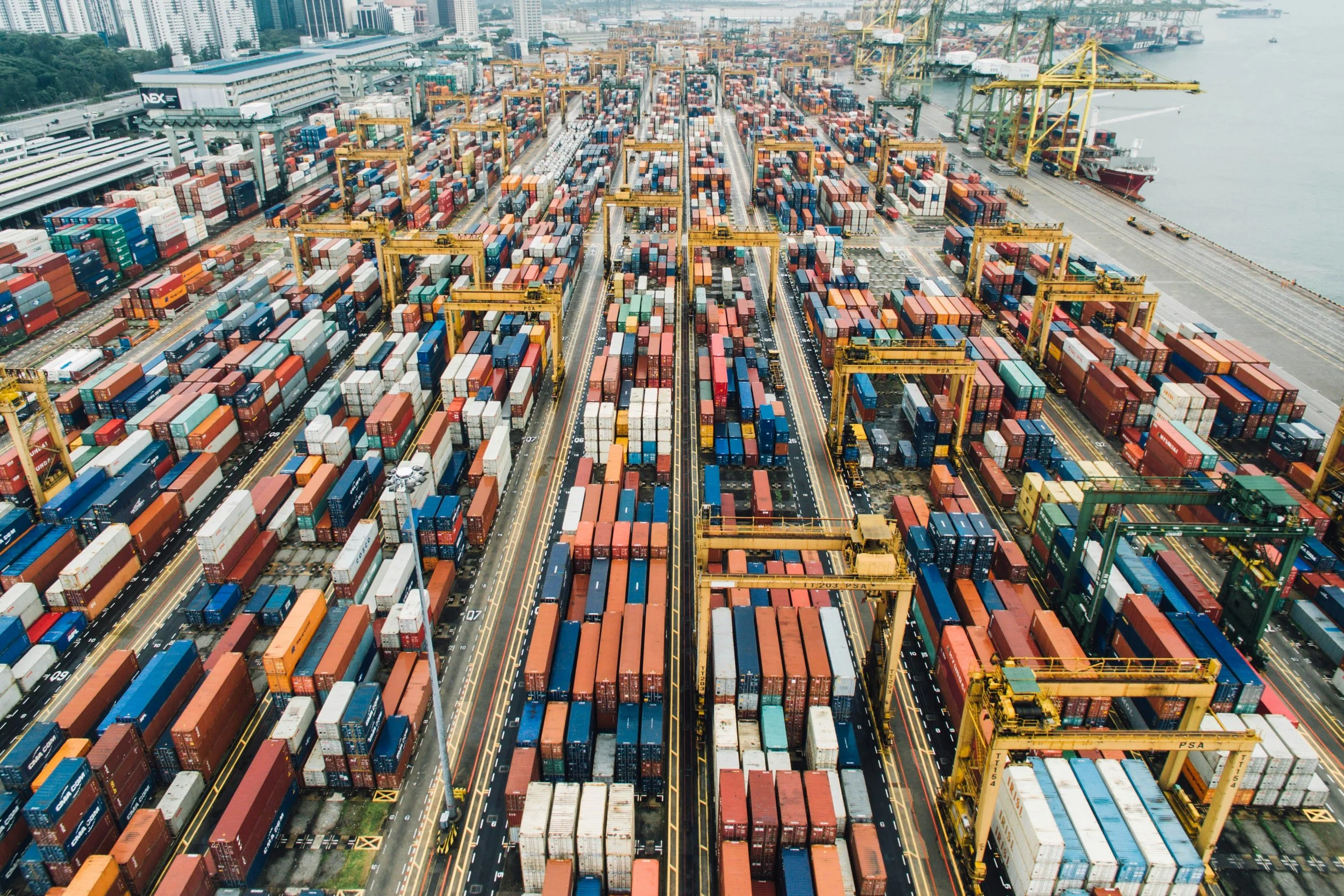 Aerial view of a shipping container yard with stacked containers and cranes.