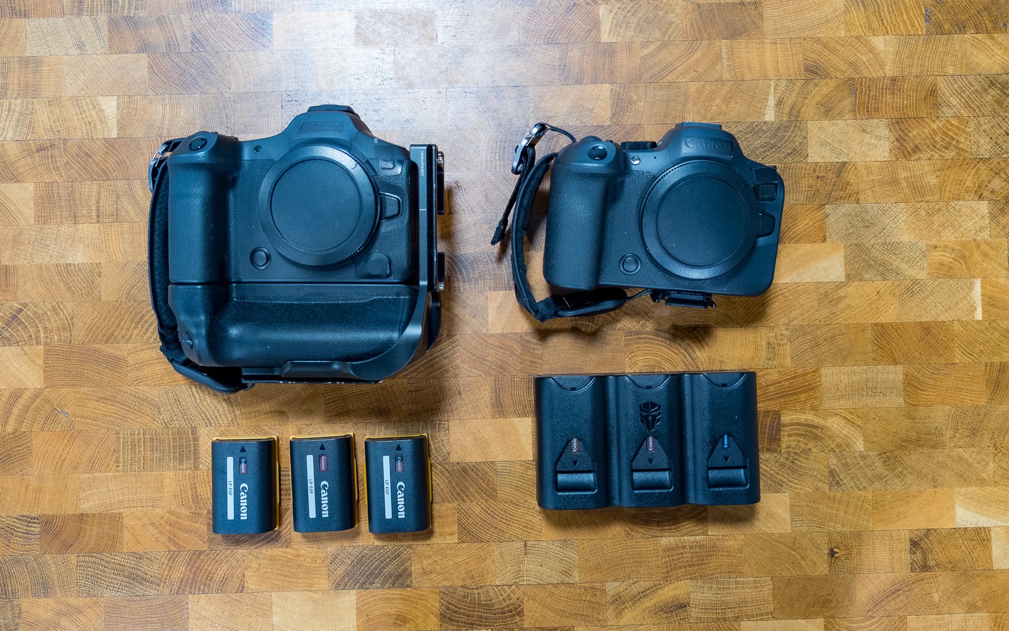 Two professional Mirrorless cameras, three Canon batteries, and a battery charger arranged on a wooden surface.