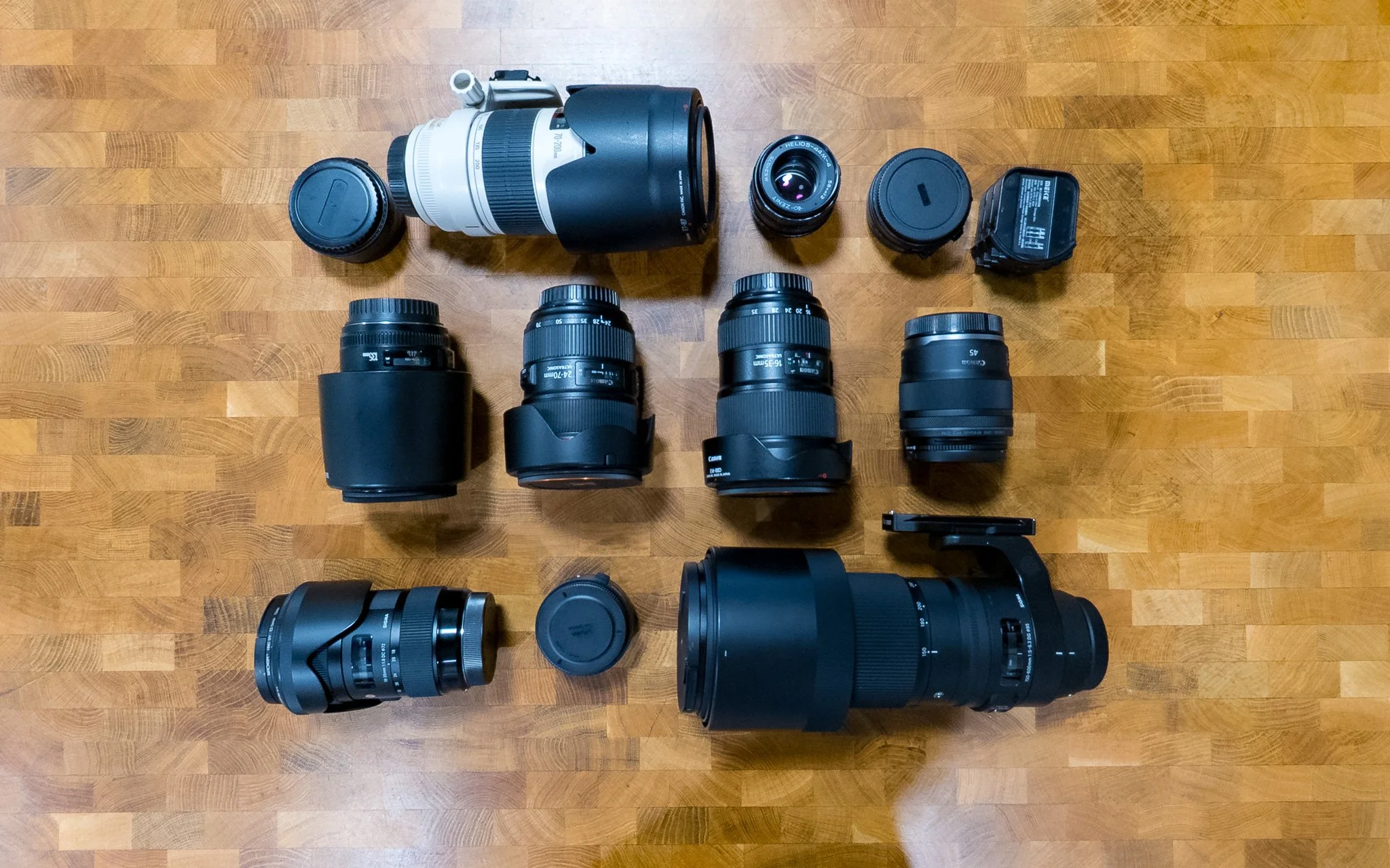 Collection of camera lenses and accessories, including telephoto zoom lens, wide-angle lens, telephoto lens, and various camera gear.
