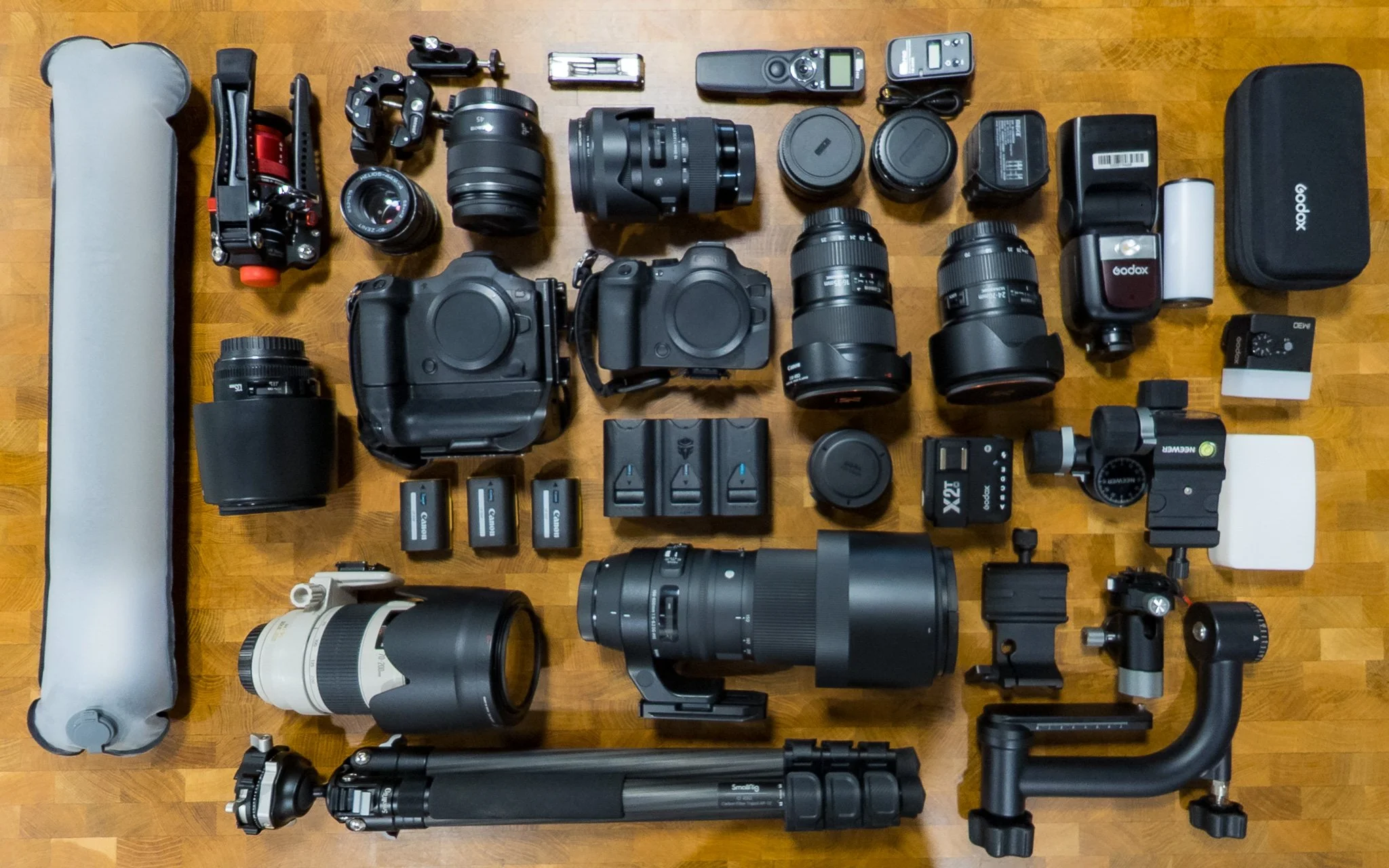 A collection of camera equipment and accessories, including lenses, cameras, batteries, chargers, a tripod, filters, and various electronic devices.