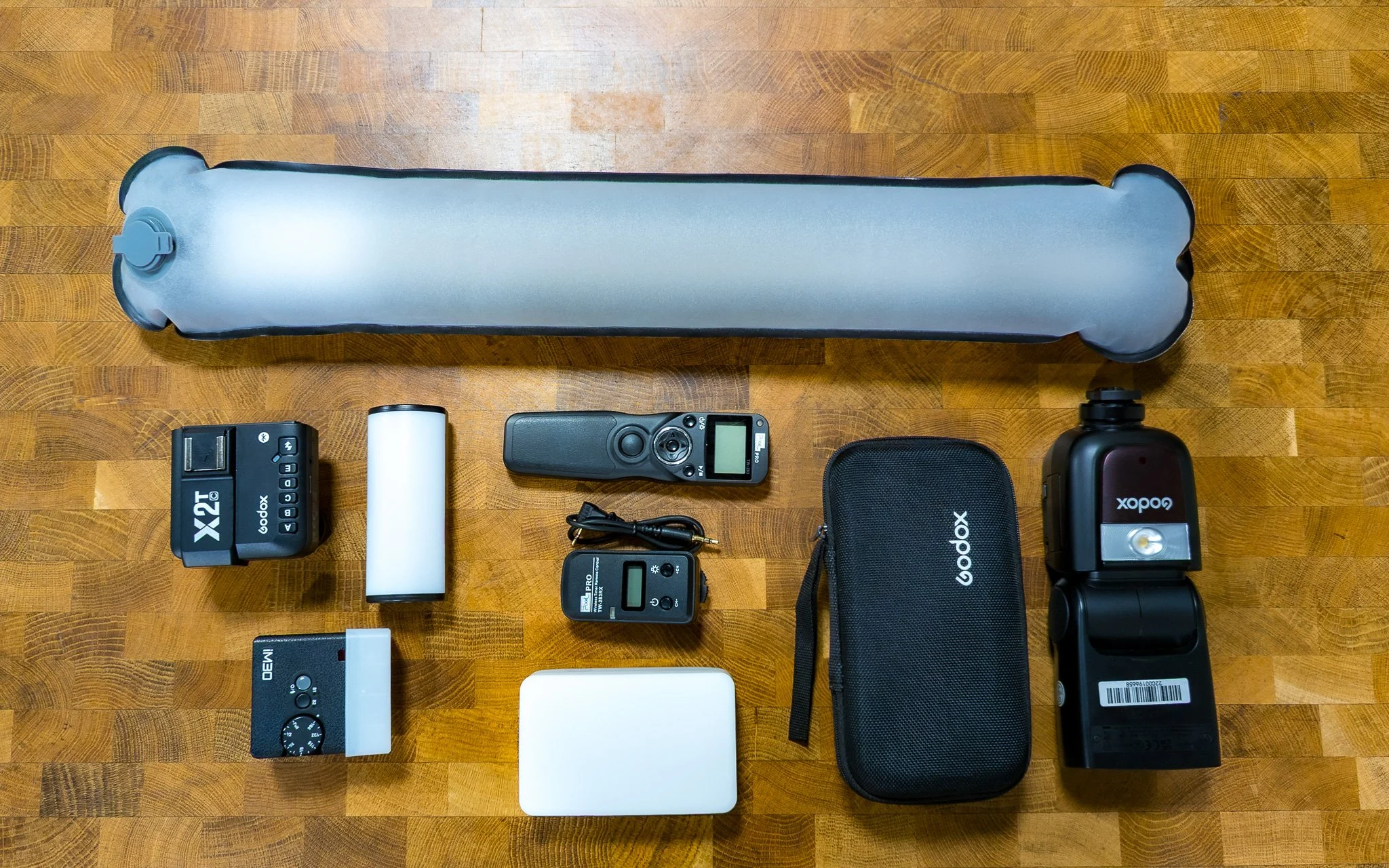 Photography lighting equipment including an inflatable tube light, two Godox speedlights, a white reflector, camera triggers, a black carrying case, and related accessories.