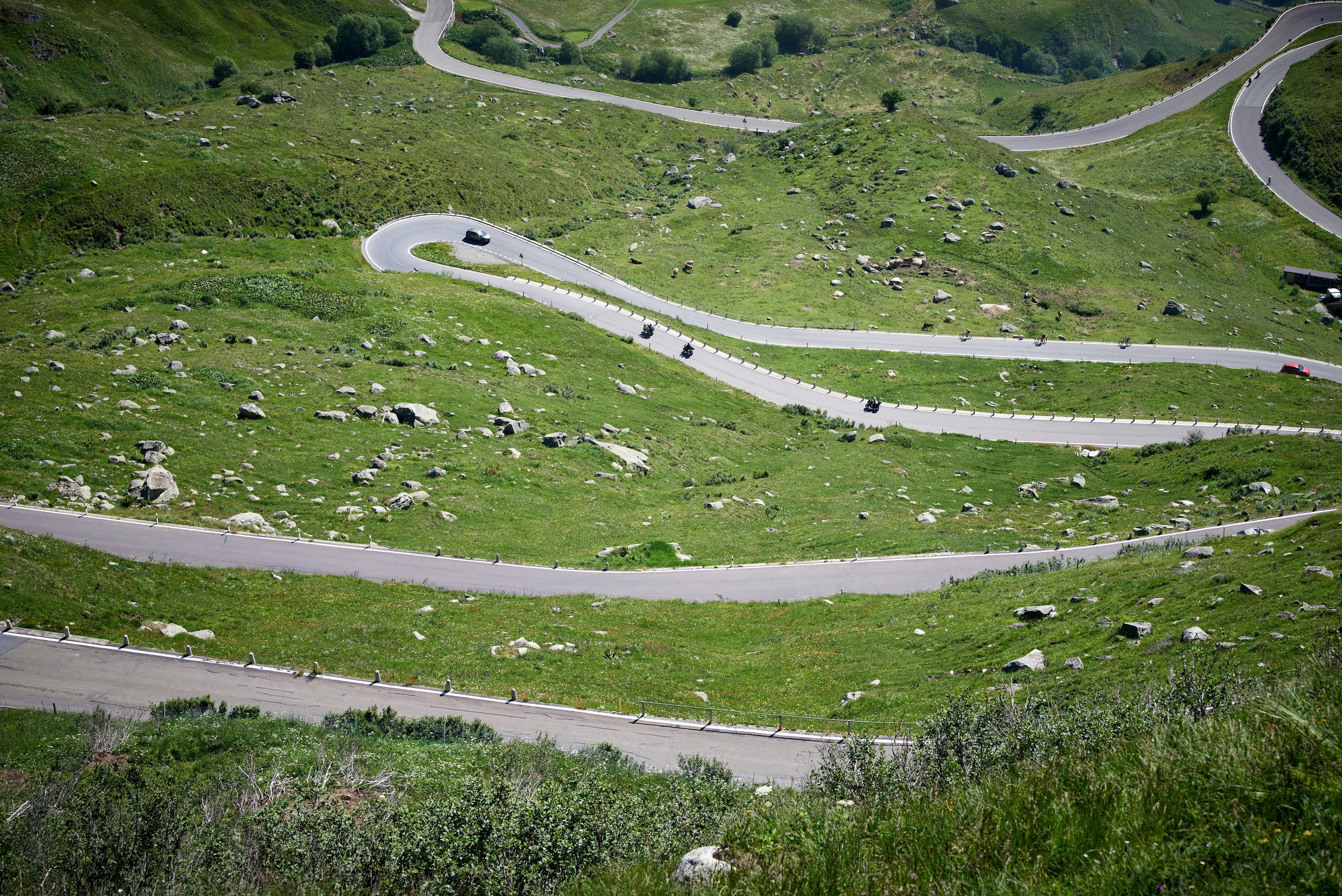 A winding mountain road with cars and motorcycles traveling through green hilly terrain.
