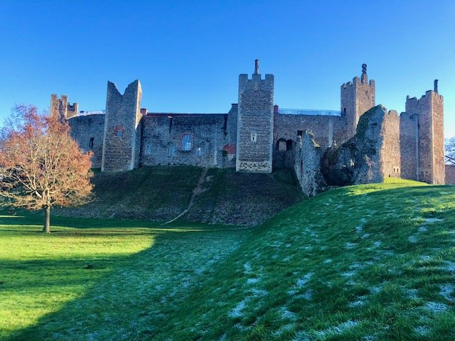 A large stone medieval castle with multiple towers sits atop a grassy hill under a clear blue sky.