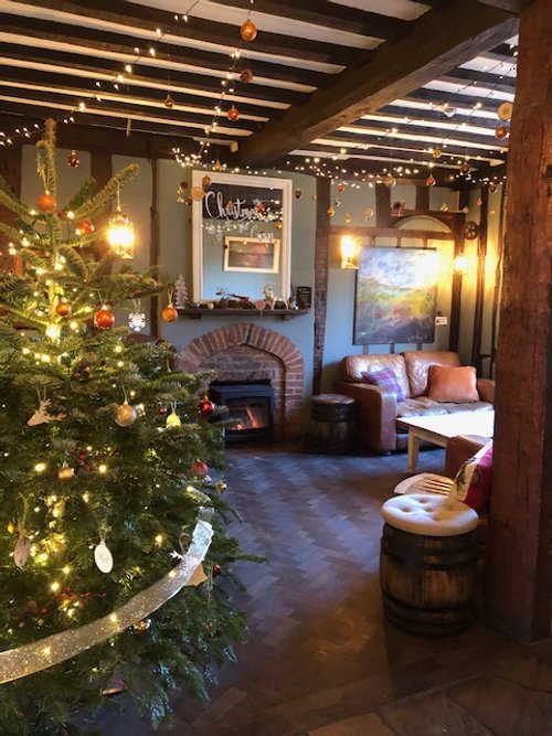 Cozy living room decorated for Christmas with a decorated Christmas tree, string lights, and festive ornaments, featuring a brick fireplace, leather sofa, and wall art.
