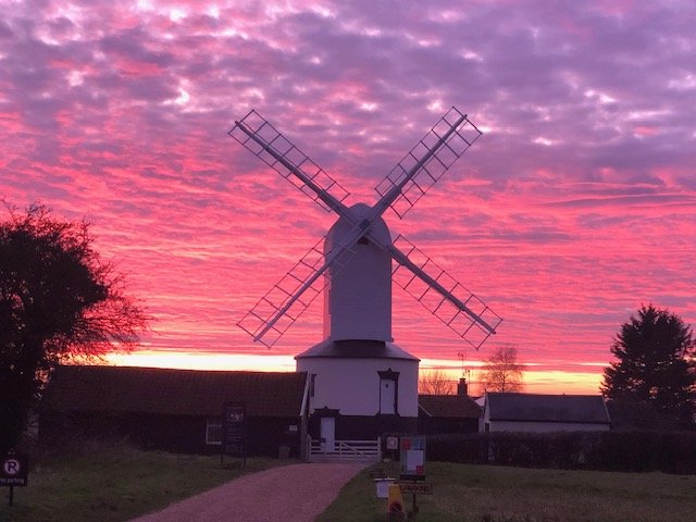A windmill with four blades in front of a vibrant pink, purple, and orange sunset sky.