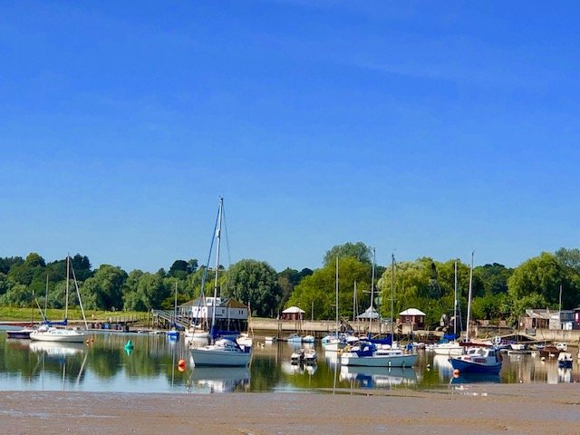 Boats docked at a marina along a calm waterway with green trees and blue sky in the background.