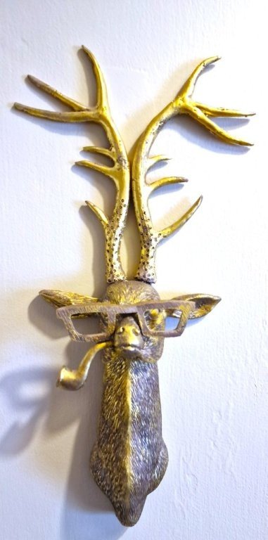 Decorative wall hanging shaped like a deer's head with antlers, glasses, and a beard, painted in gold and silver tones.