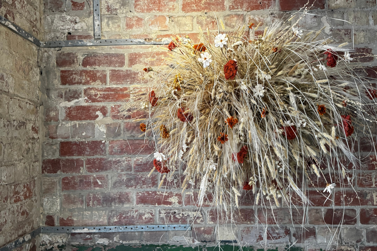 wall hanging of dried grasses and flowers against old red brickwork